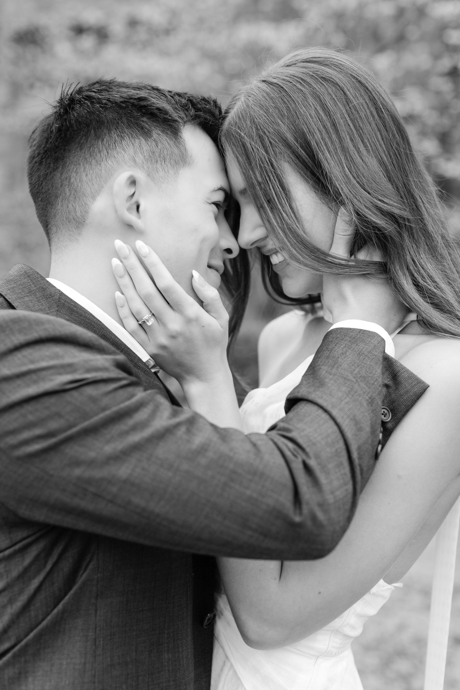 A romantic black and white portrait of a couple sharing an intimate moment outdoors, with foreheads touching. Goodwin Manor.