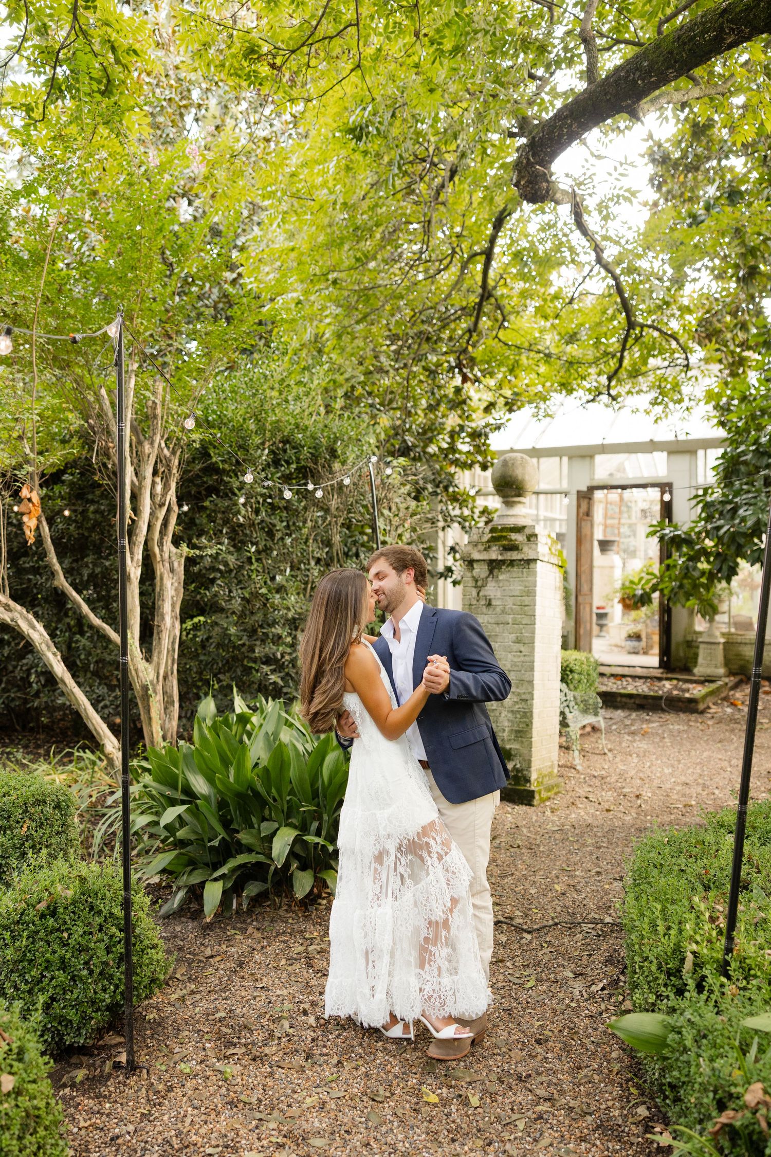 A romantic couple embraces on a garden path surrounded by lush greenery and a decorative archway.