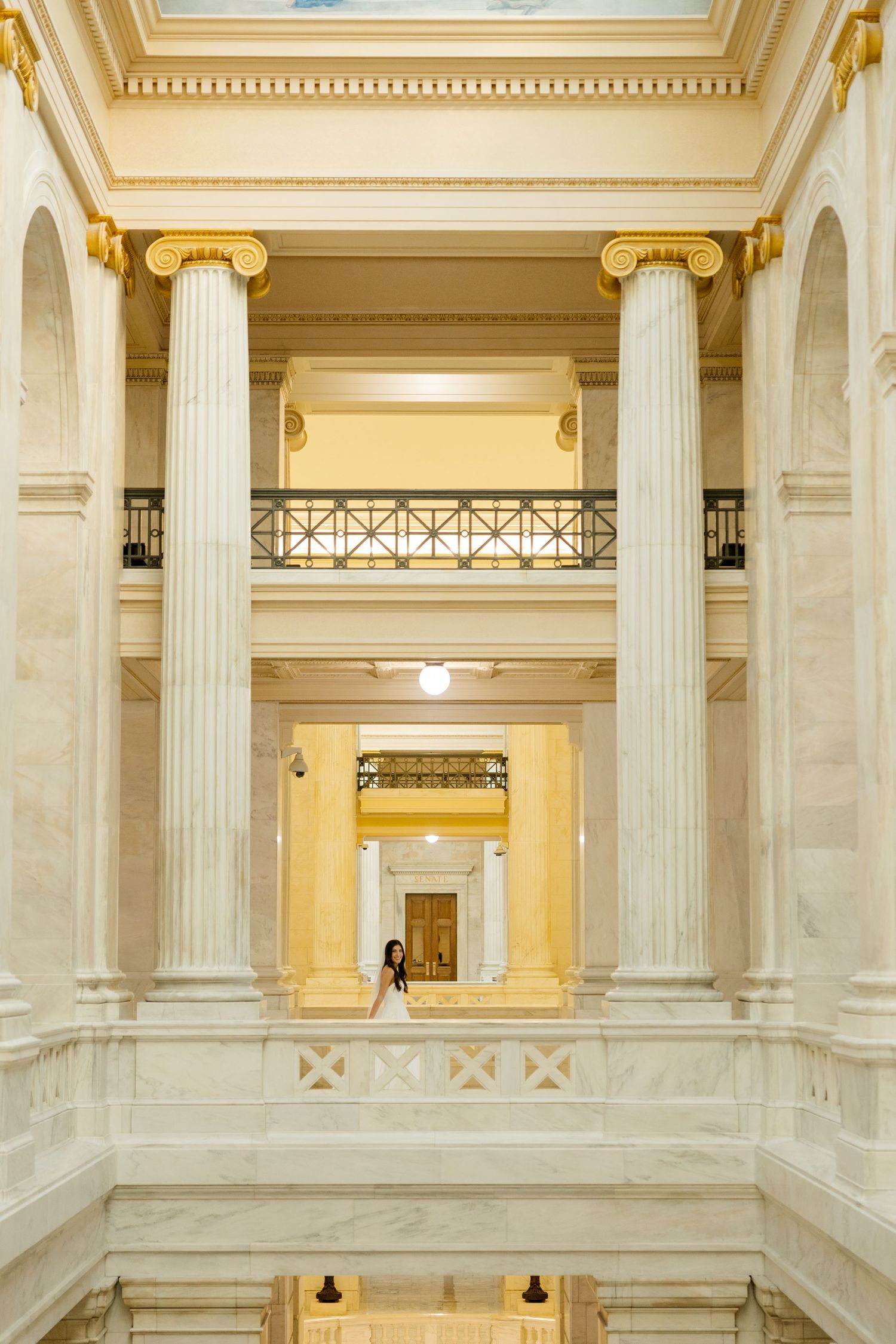 Interior view of a grand neoclassical building with white marble columns and ornate gold trim details.