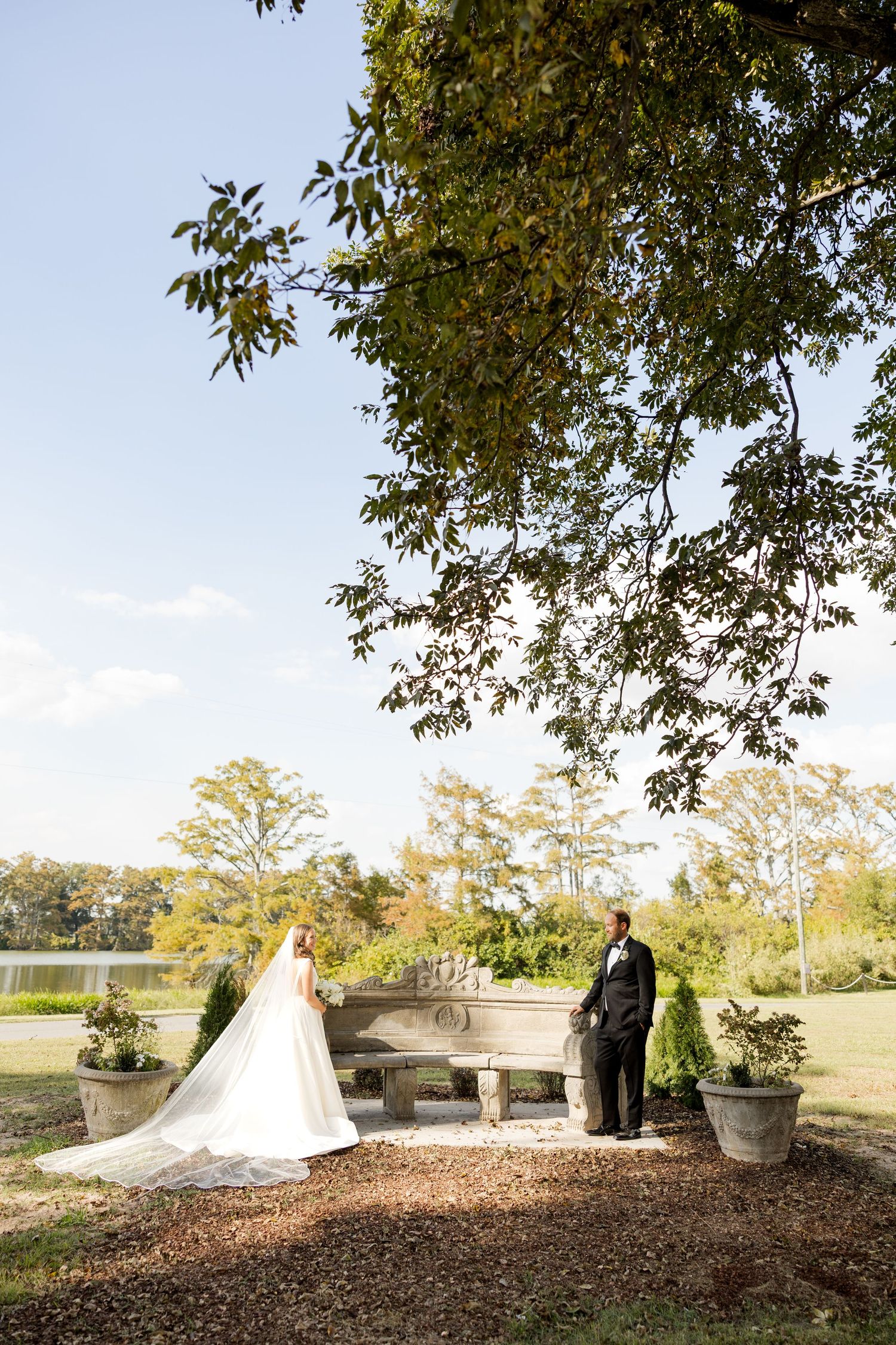 Wedding ceremony setup under large trees with white chairs and floral arrangements on a fall day.