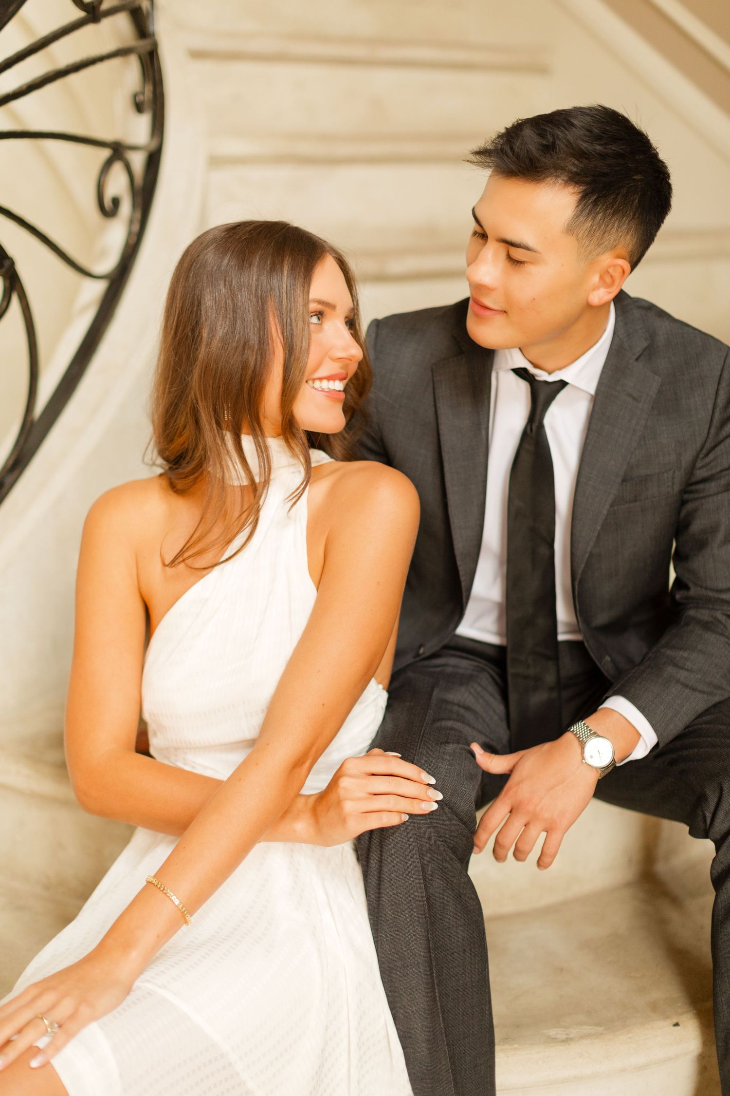 A couple in formal attire sits close together on stone steps during an engagement photoshoot. Goodwin Manor.