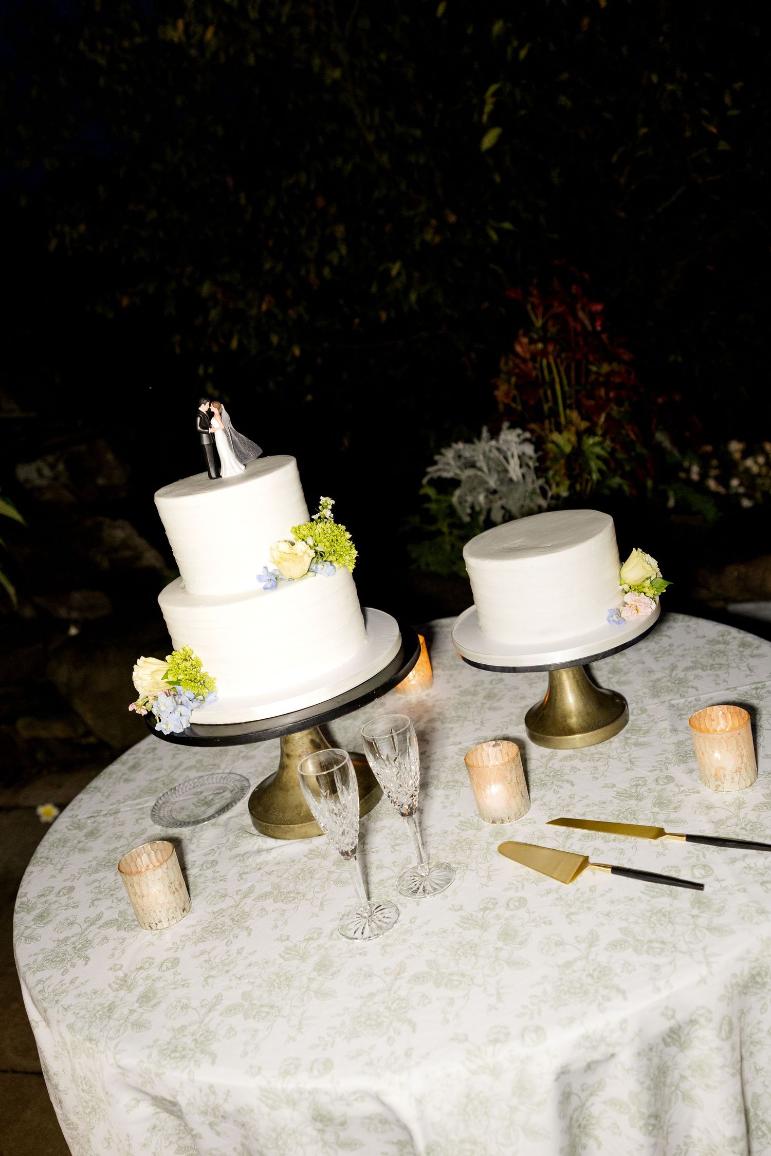 Elegant white wedding cakes displayed on a lace-covered table with gold accents and floral decorations.Botanical Gardens of the Ozarks