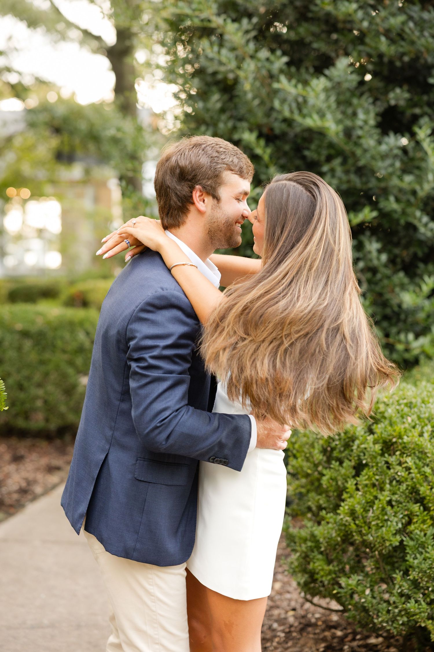 A couple sharing an intimate moment outdoors against a backdrop of green foliage.