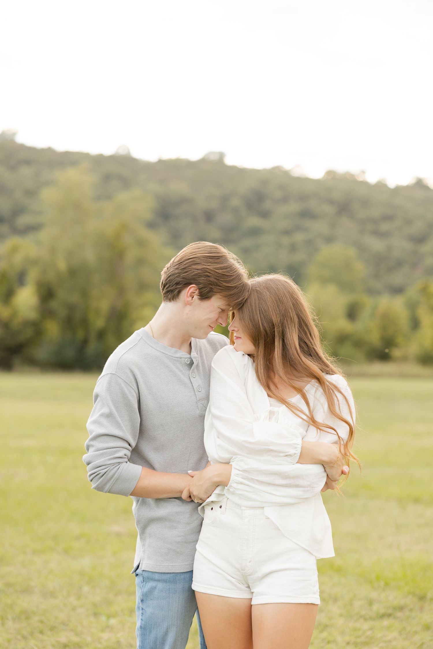 A playful couple embracing in a sunlit meadow wearing casual clothing.