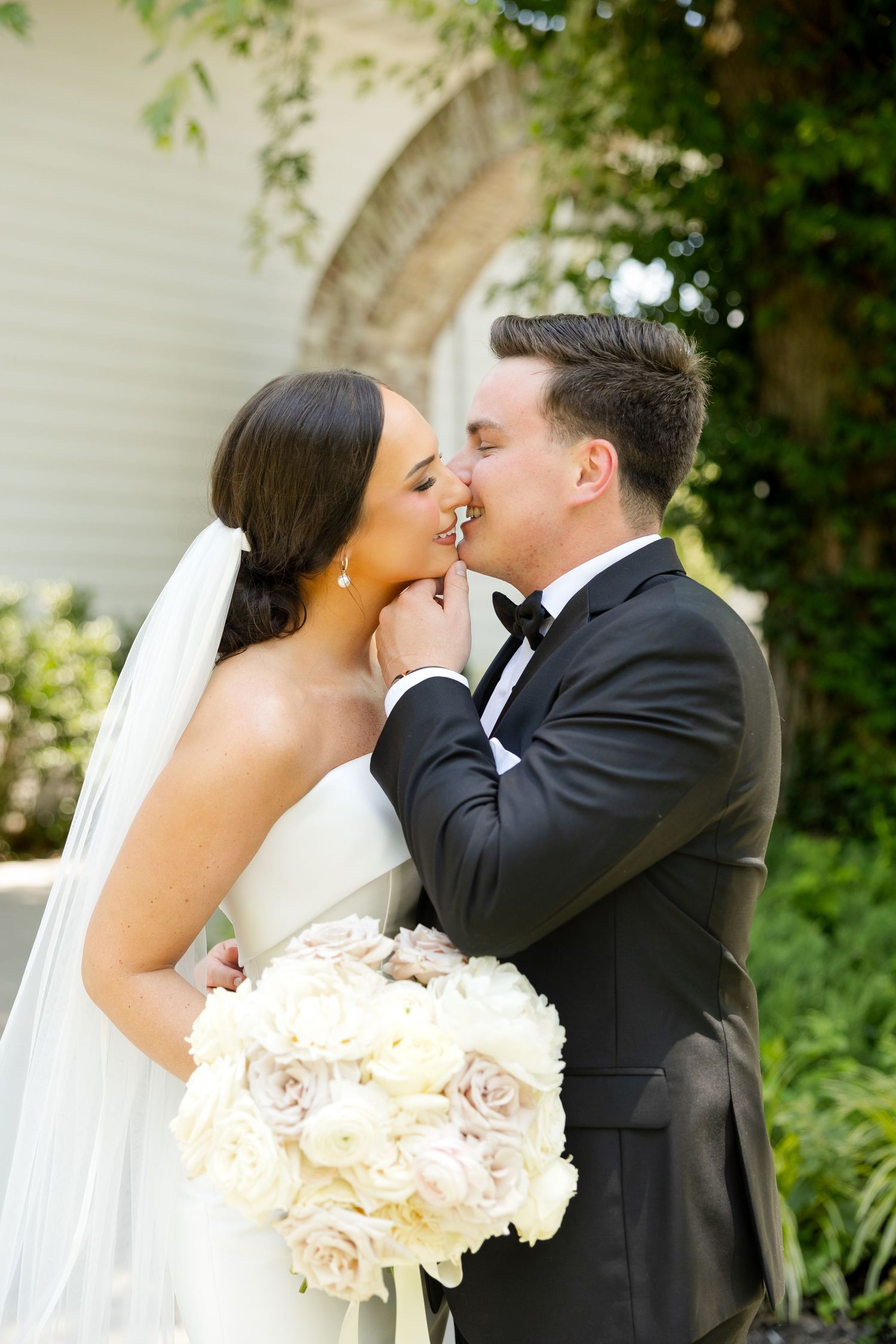A romantic wedding moment with a beautiful bouquet of blush roses as the newlyweds share a tender kiss in a garden setting.