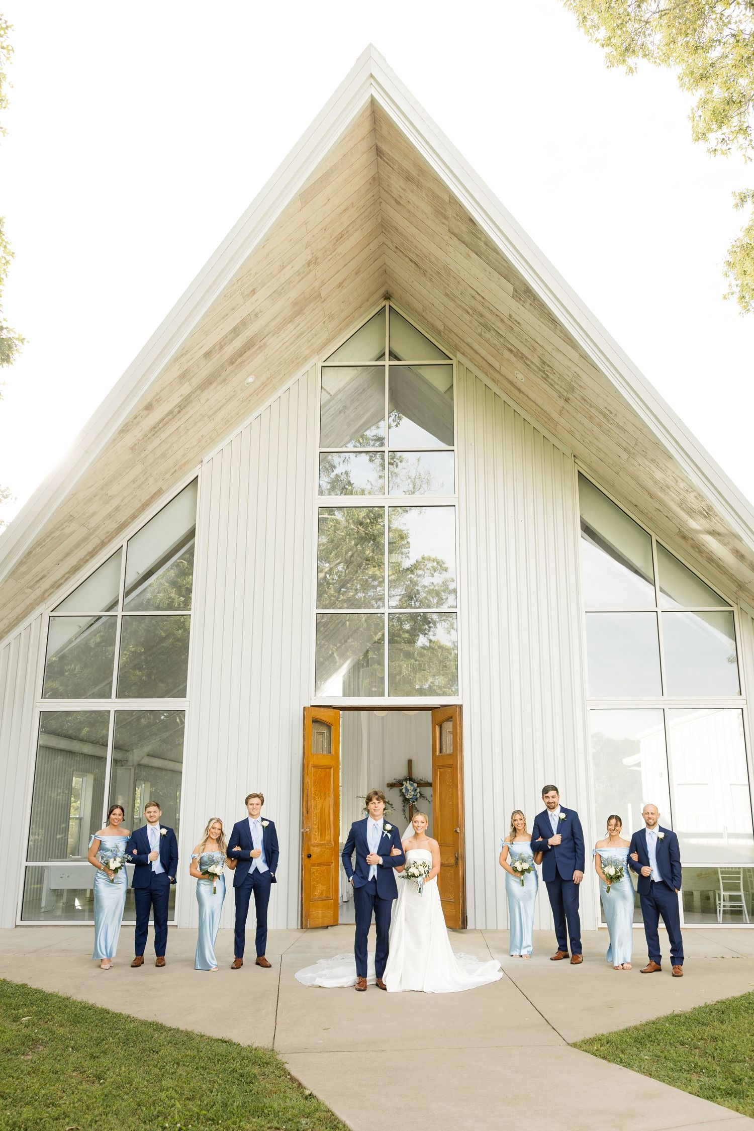 A wedding party poses outside a modern white chapel building with angular architecture.Cold Springs Events.