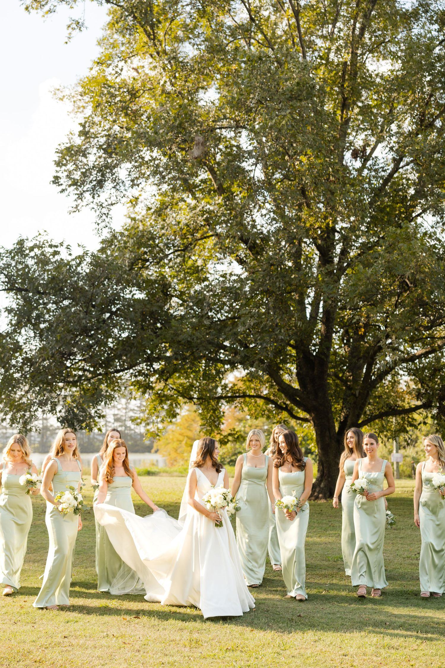A group in white dresses poses together outdoors under tall trees in golden sunlight.Marlgsate Plantation