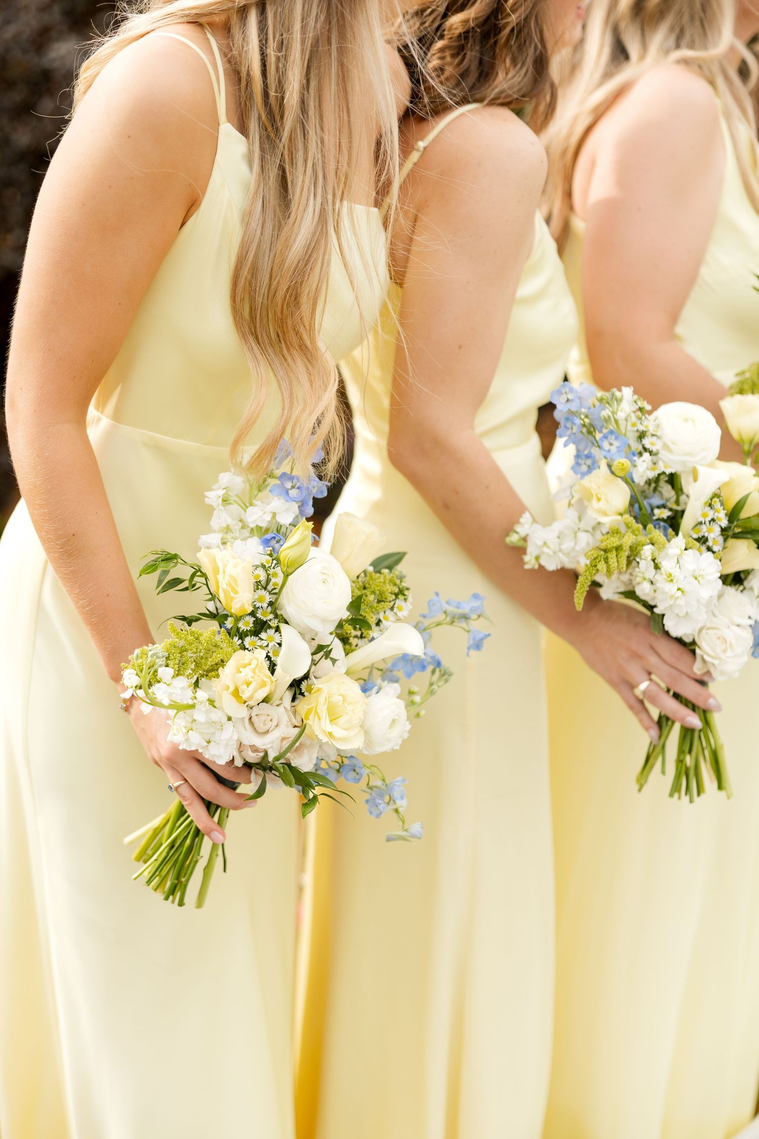 Row of bridesmaids in pale yellow dresses holding delicate white and blue floral bouquets.Botanical Gardens of the Ozarks