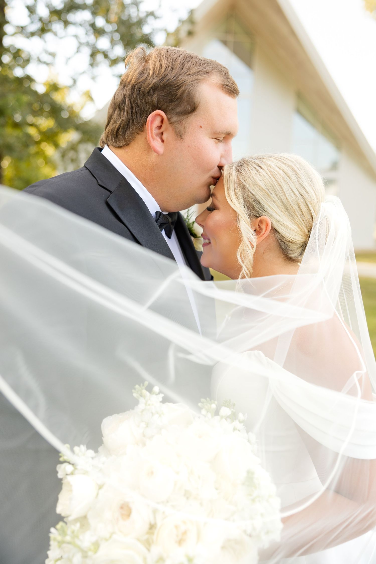 Wedding couple shares an intimate kiss while holding a white bouquet outside a chapel. Cold Springs Events.