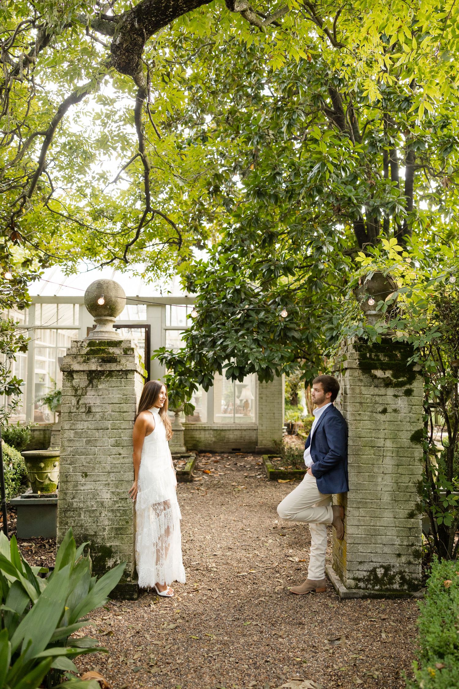 Couple walking along a garden path with stone pillars and lush greenery during an outdoor photo session.