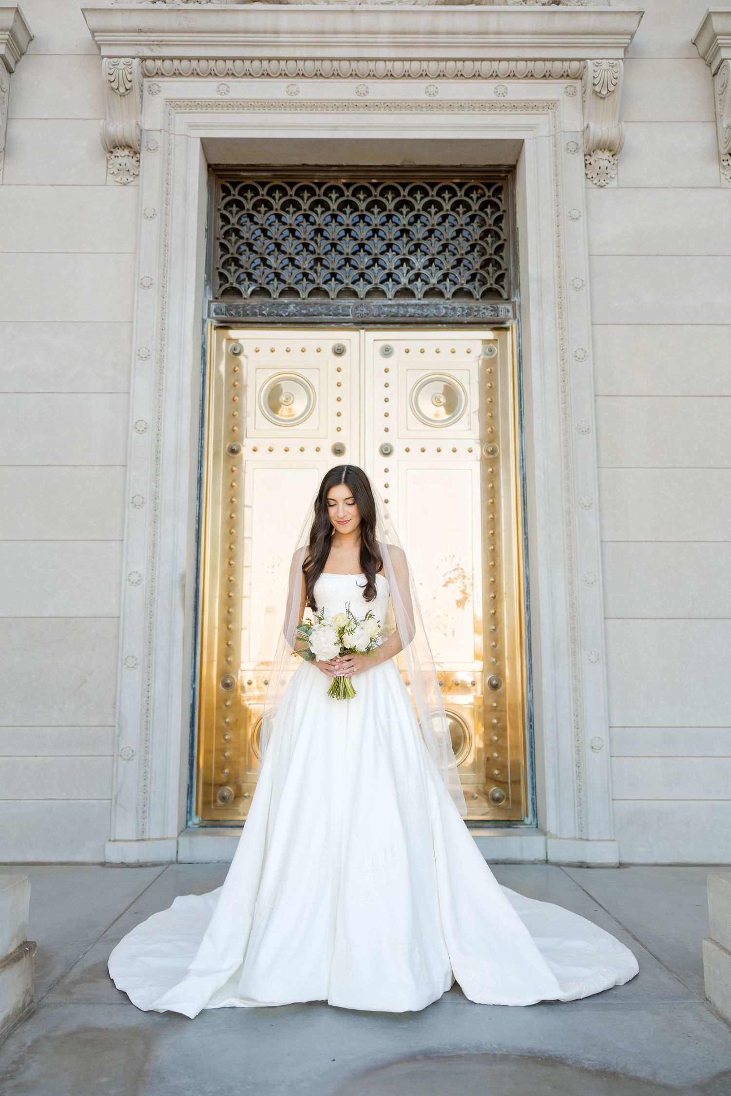 Elegant white wedding gown photographed against ornate gold doors and stone architecture.