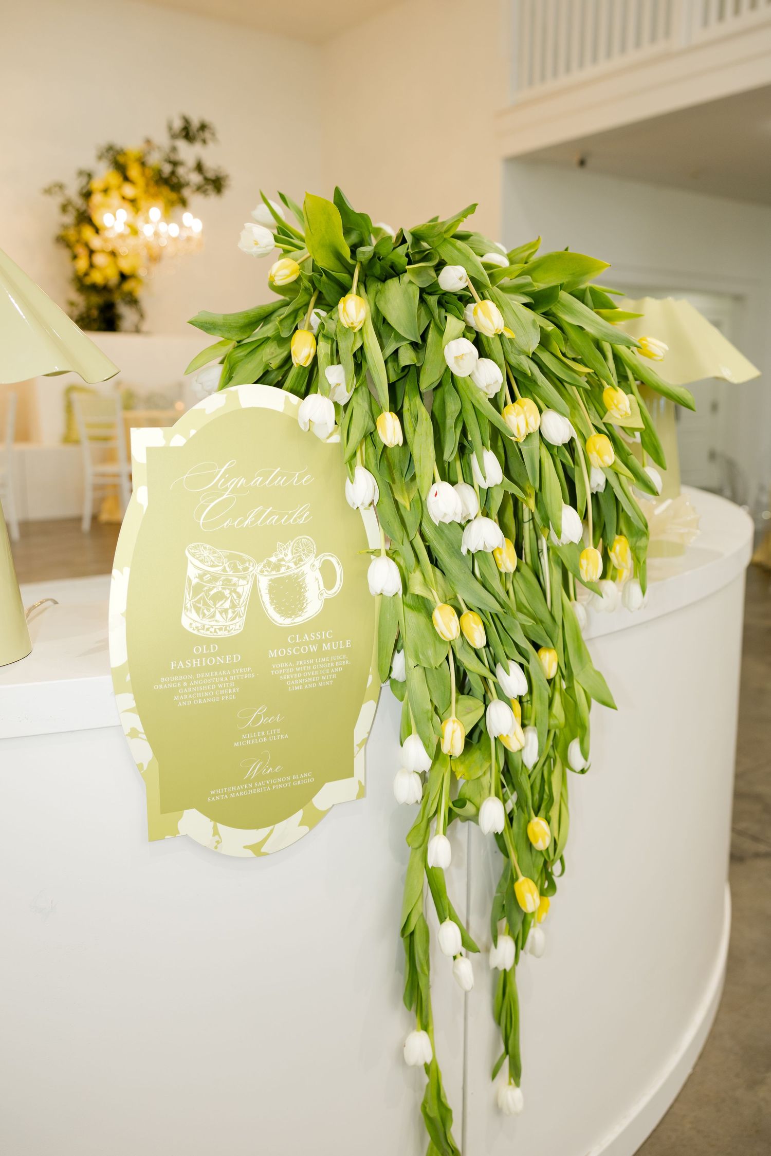 Elegant bar display adorned with cascading yellow and white tulips next to a signature cocktails sign.