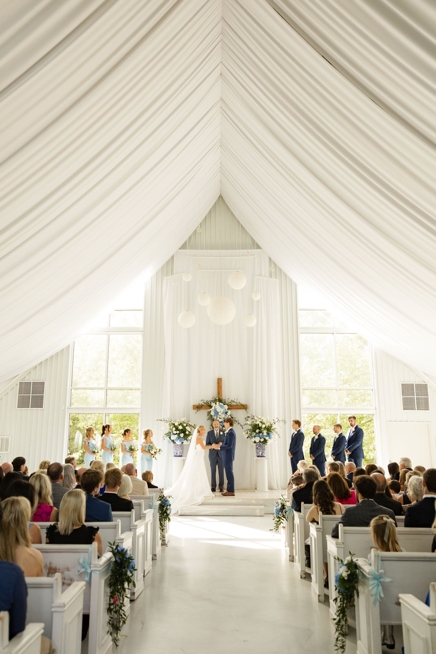 A white chapel filled with guests during a wedding ceremony with draped fabric ceiling.Cold Springs Events.