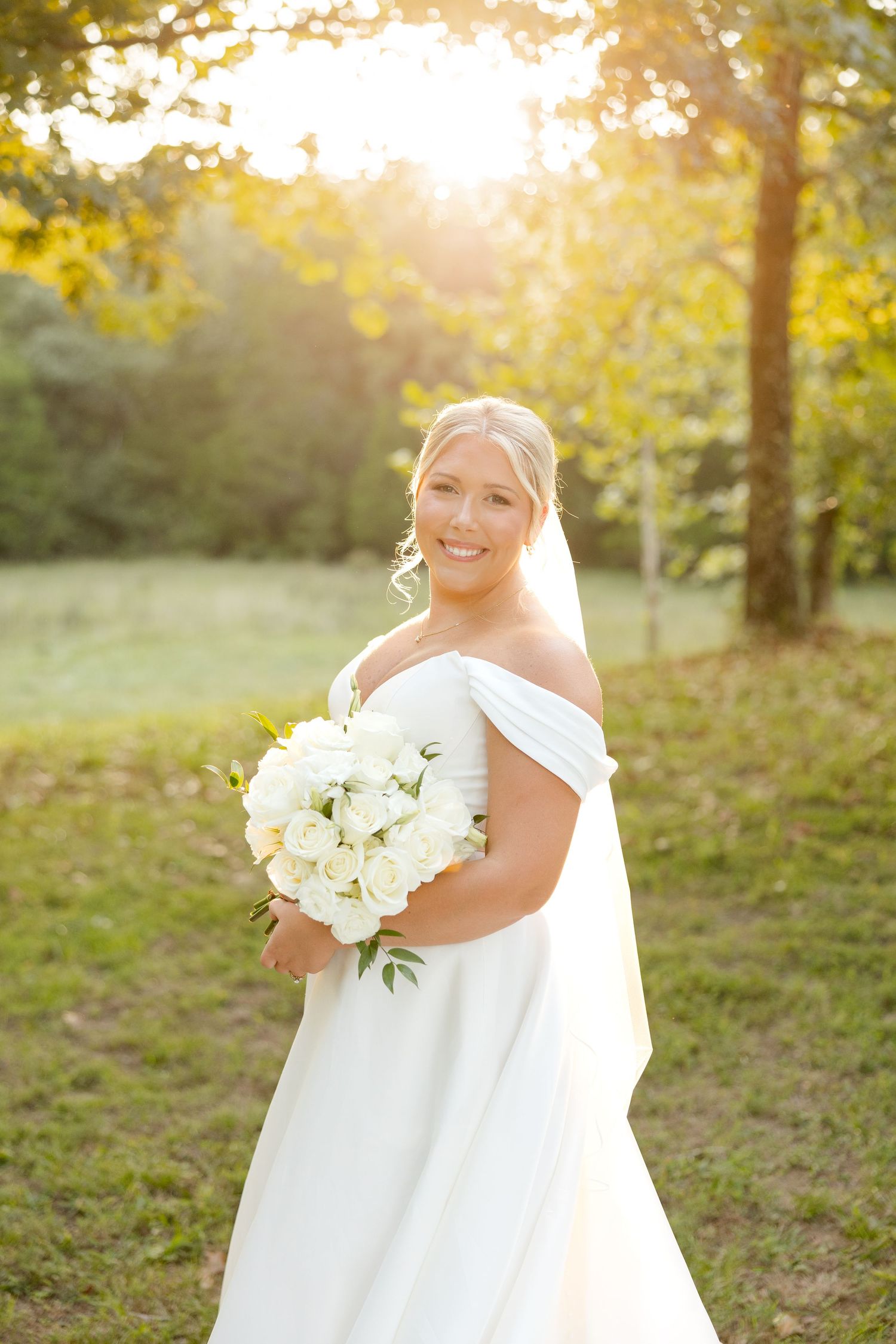 A bride holds a white bouquet during golden hour outdoor bridal portraits.
