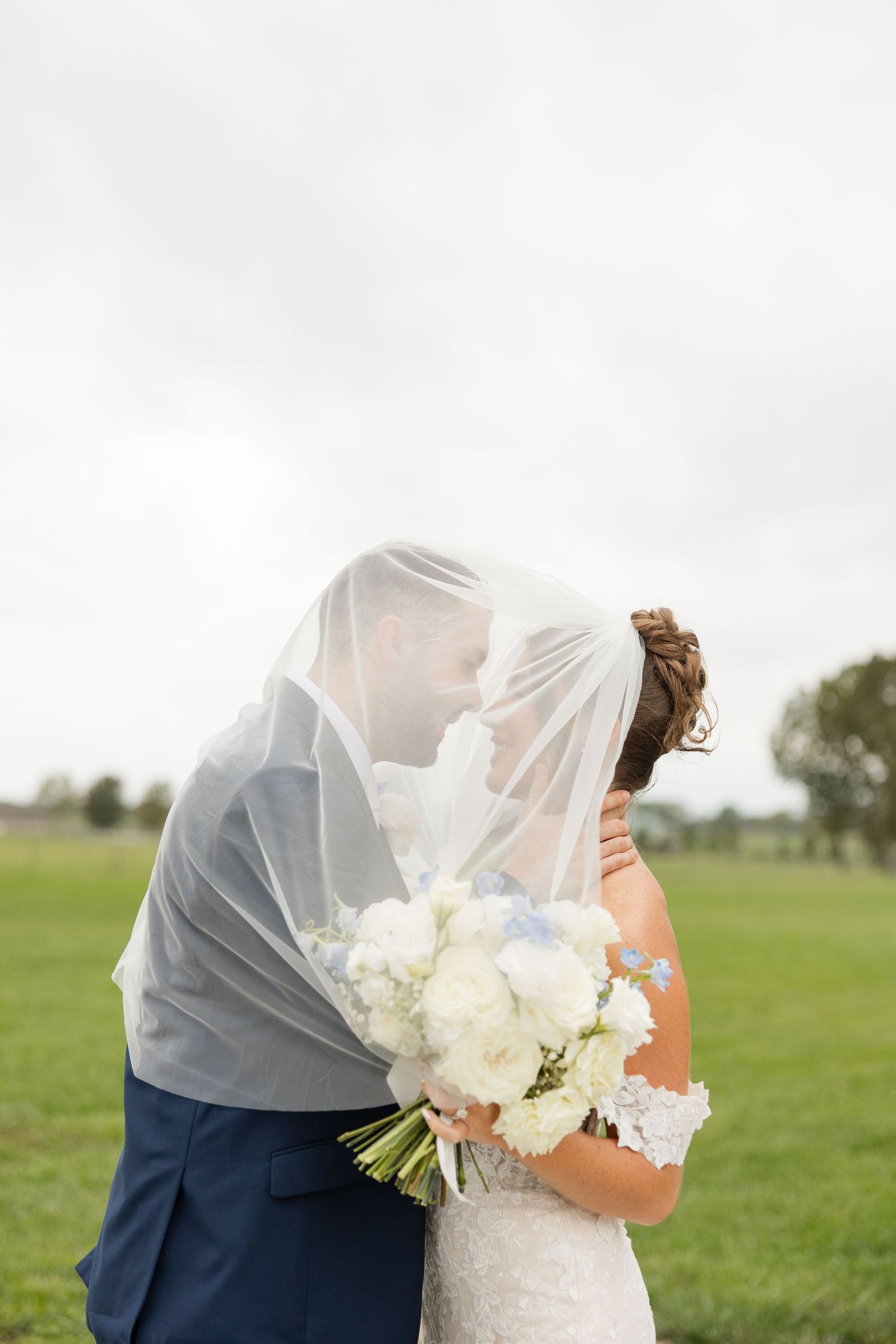 A couple shares an intimate moment under a delicate veil with white flowers in an outdoor setting.