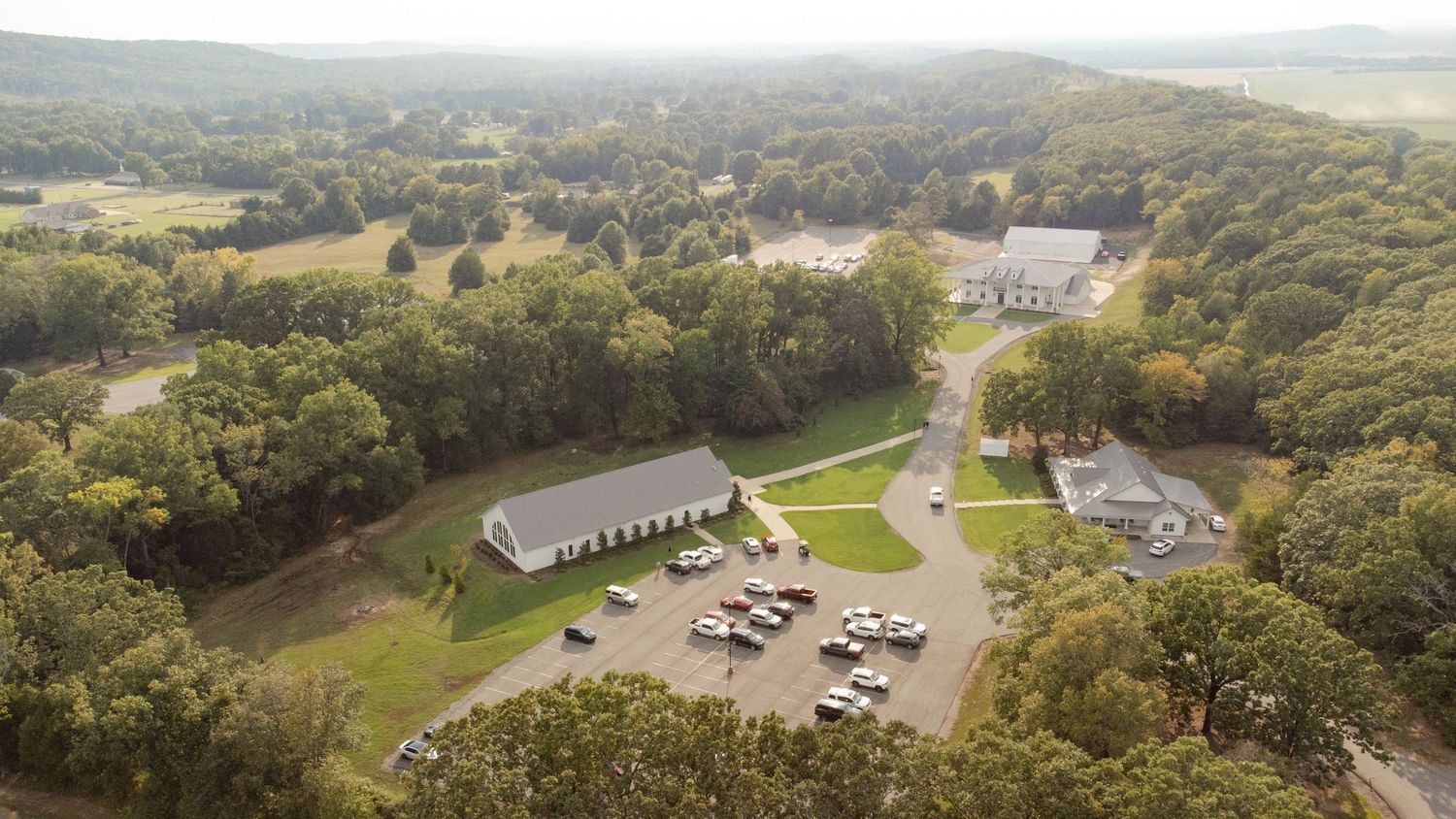 Aerial panoramic view of green rural countryside with scattered buildings and trees stretching to the horizon.