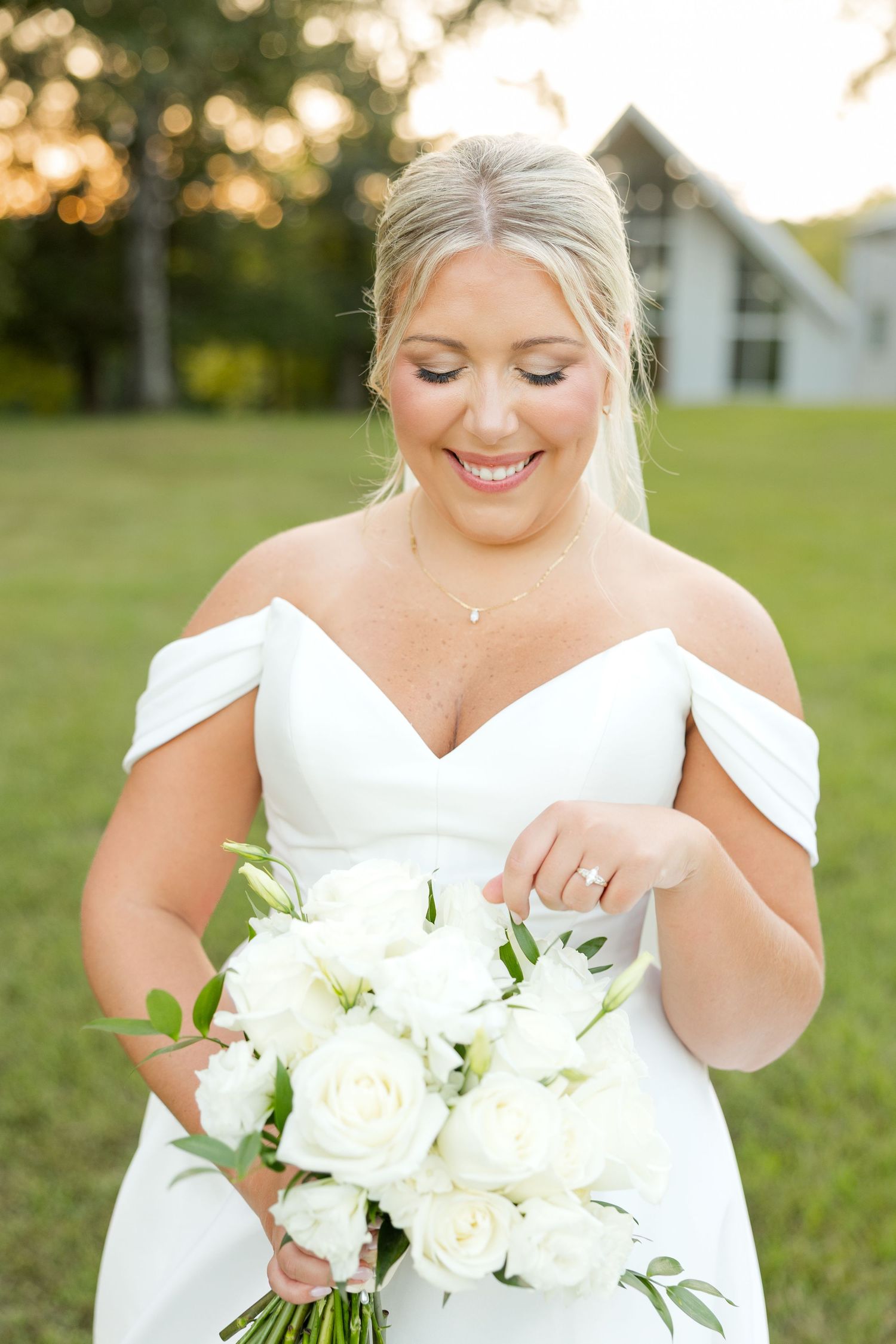 Close up details of a bridal bouquet with white roses and greenery against a soft outdoor background.
