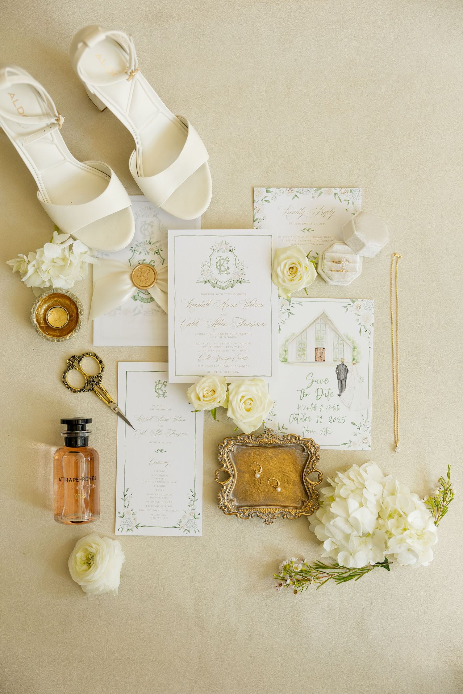 Wedding details flatlay with white sandals, invitation suite, perfume bottle, and delicate cream roses on beige background. Cold Springs.