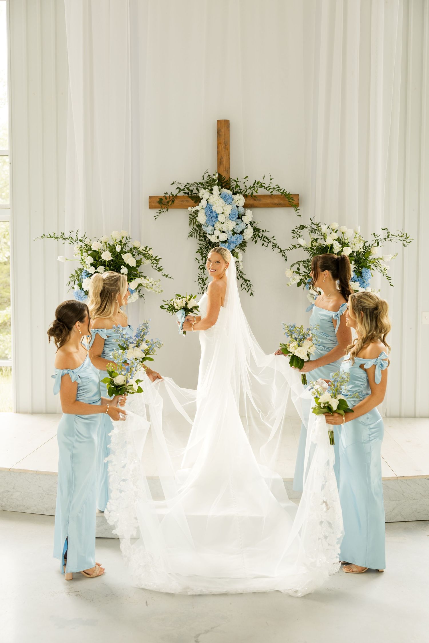 Bridesmaids in light blue dresses help arrange the bride's flowing white veil.Cold Springs Events.