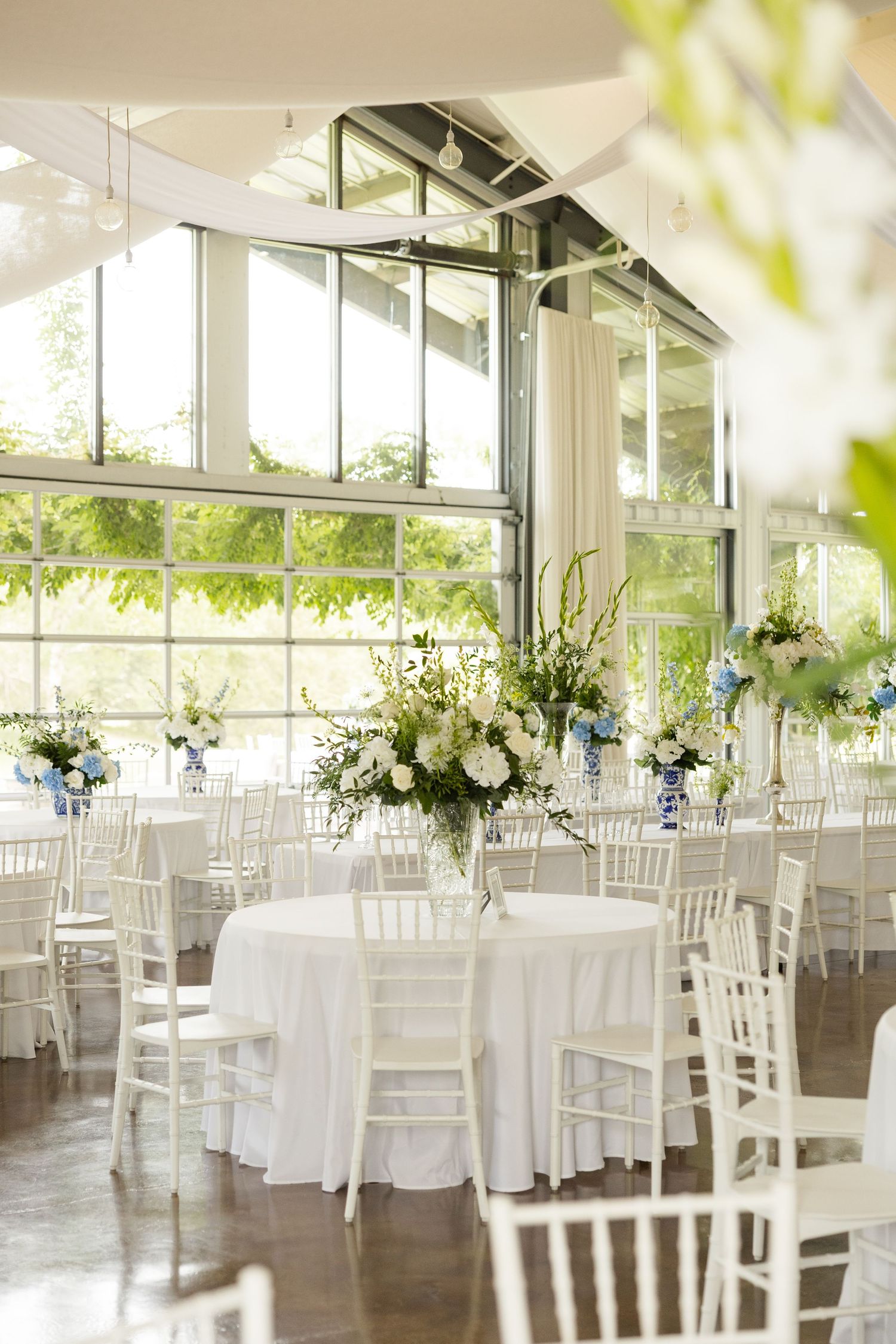 Light-filled reception venue with white chiavari chairs and floral centerpieces.Cold Springs Events