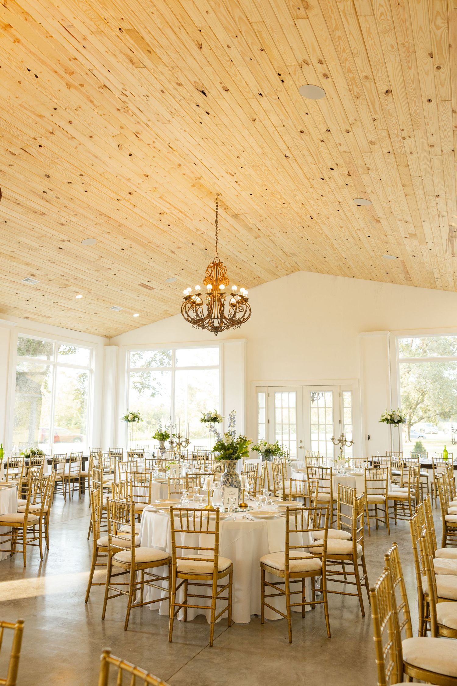 Elegant wedding reception venue with wood paneled ceiling, gold chiavari chairs, and white linens in a bright airy space.