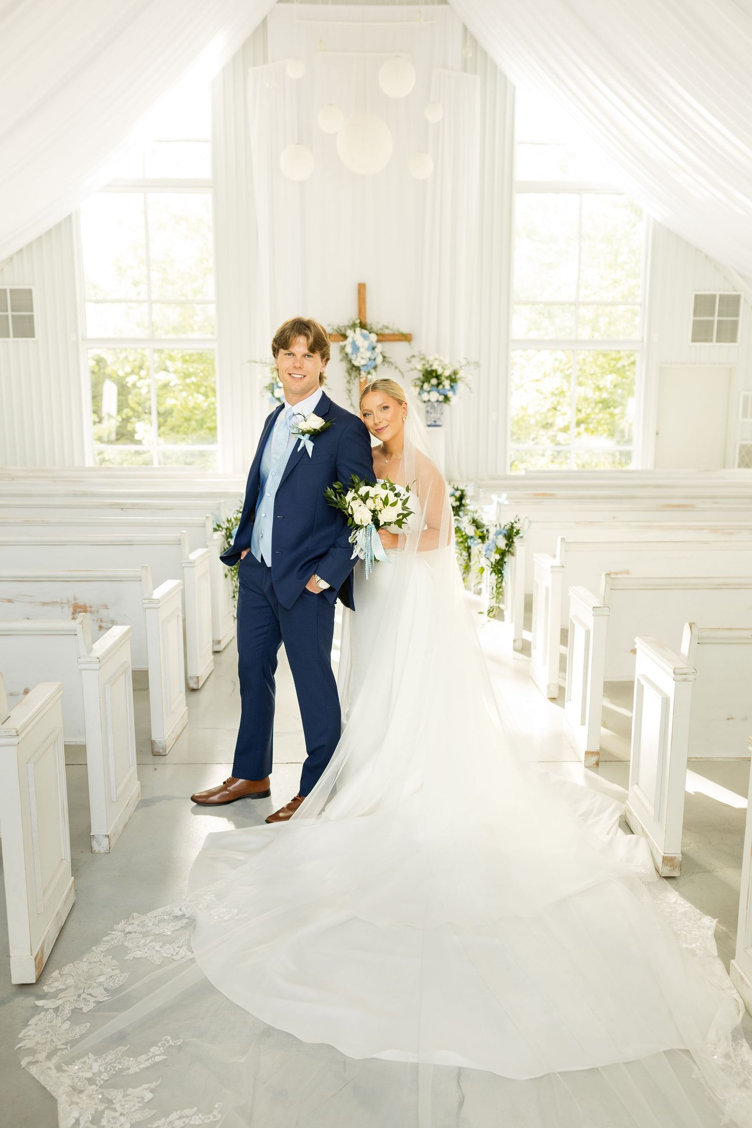Elegant wedding couple poses in bright white chapel with natural light streaming through windows.Cold Springs Events