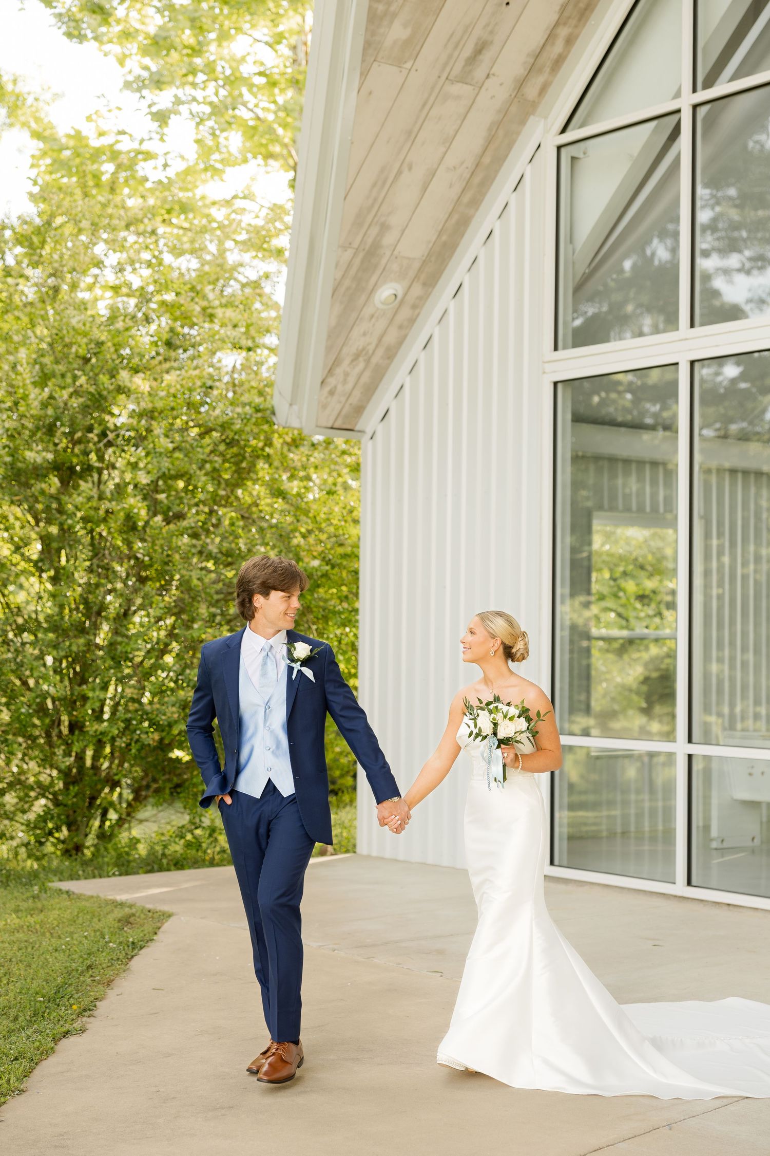 Wedding couple poses playfully outside a modern white building with large windows. Cold Springs Events.