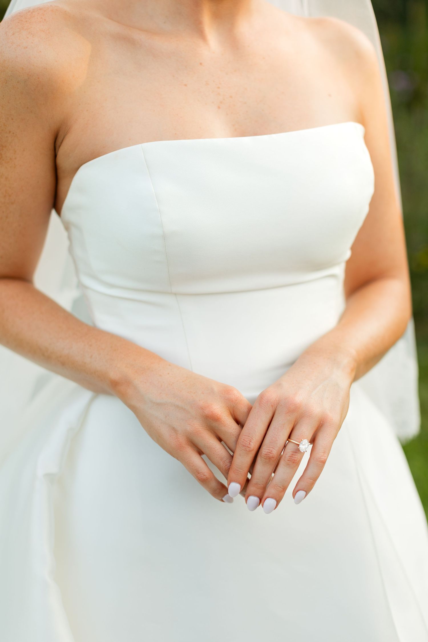 Close-up details of a strapless white wedding dress bodice showing delicate fabric and clasped hands.