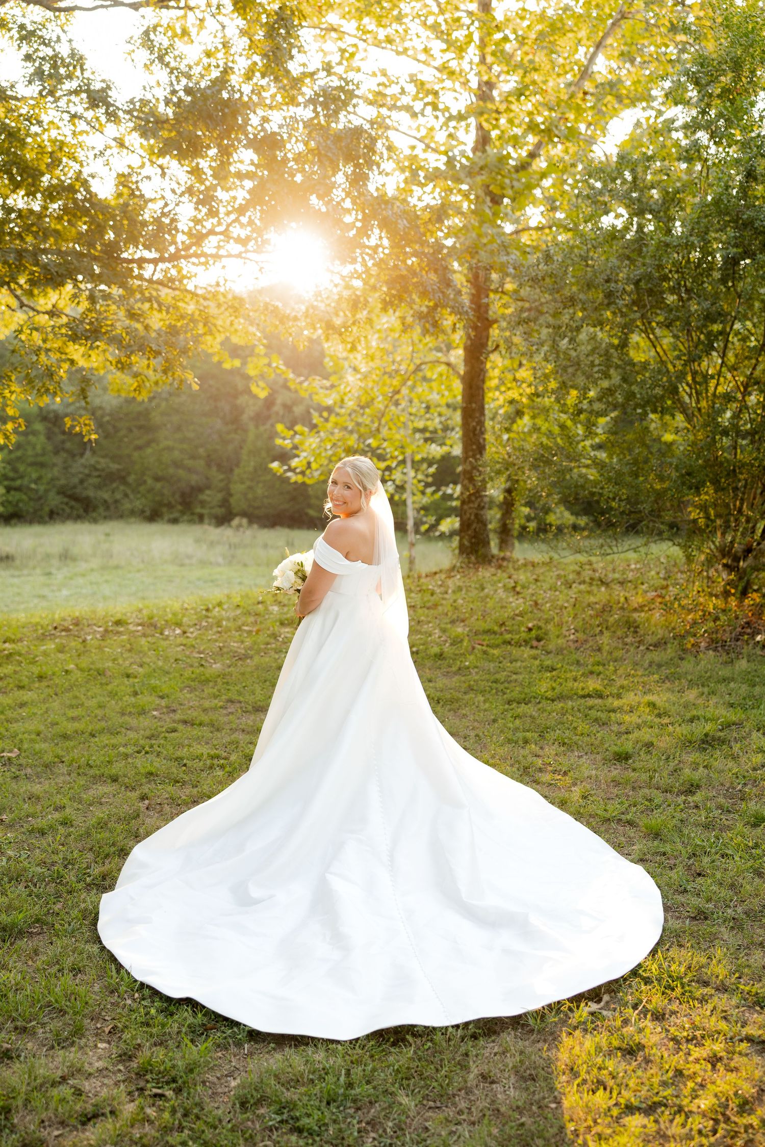 A stunning white wedding dress with long train photographed during golden hour in a natural outdoor setting.