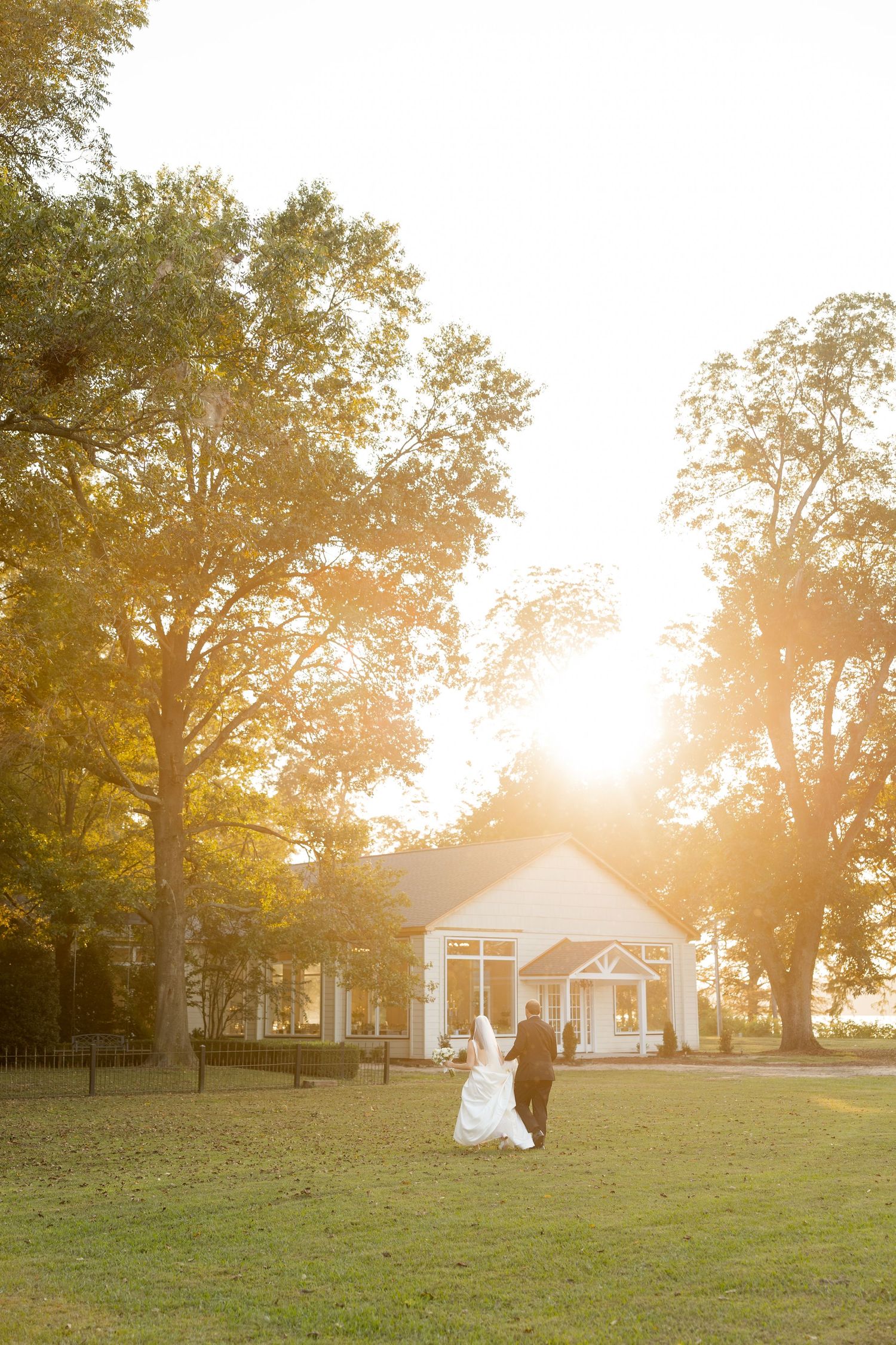Golden sunset illuminates a rustic white chapel and lawn creating a dreamy wedding ceremony backdrop.