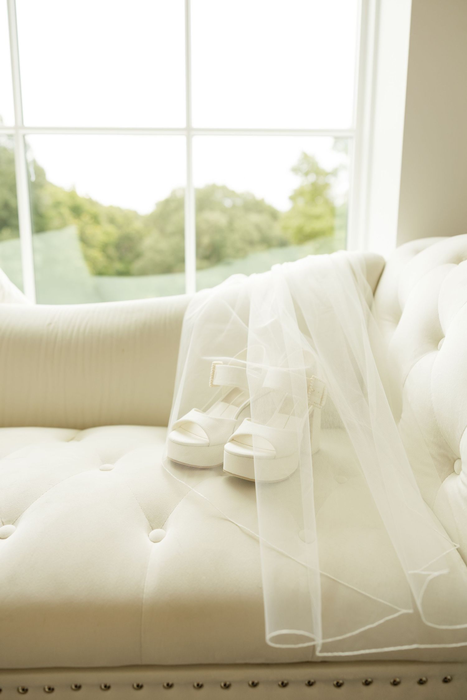 Delicate white wedding veil draped over an upholstered couch near a bright window. Grand at the Springs.