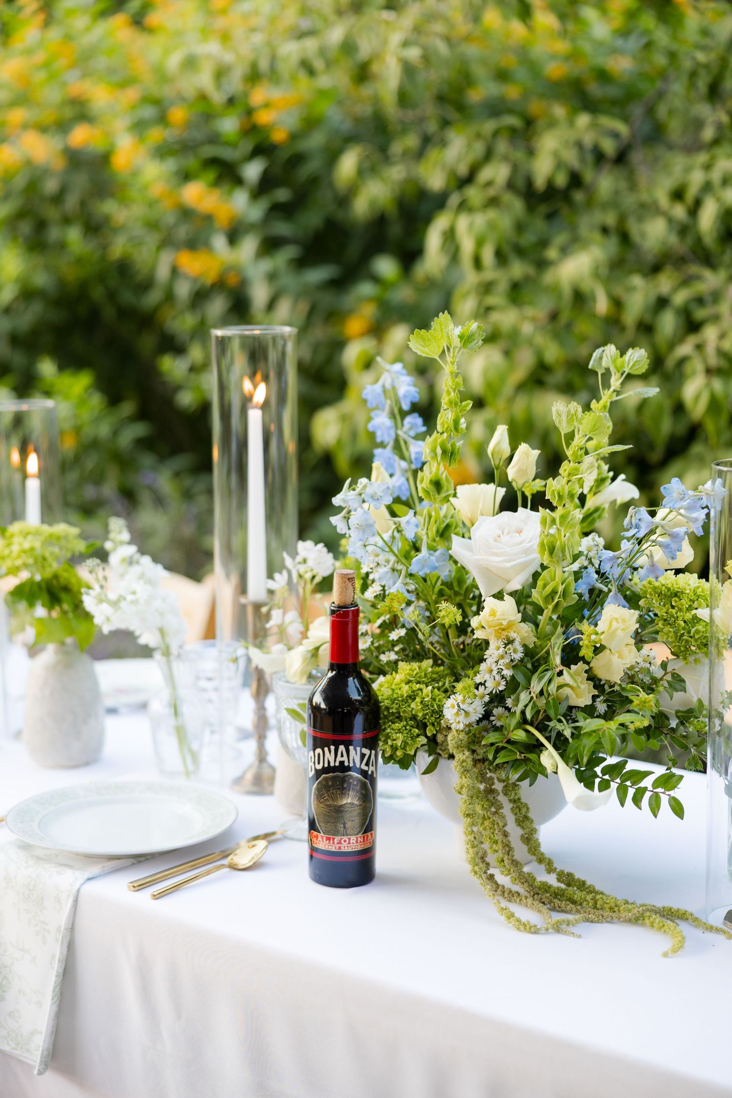 Wedding reception table with blue and white floral arrangements, candles, and wine bottle.Botanical Gardens of the Ozarks
