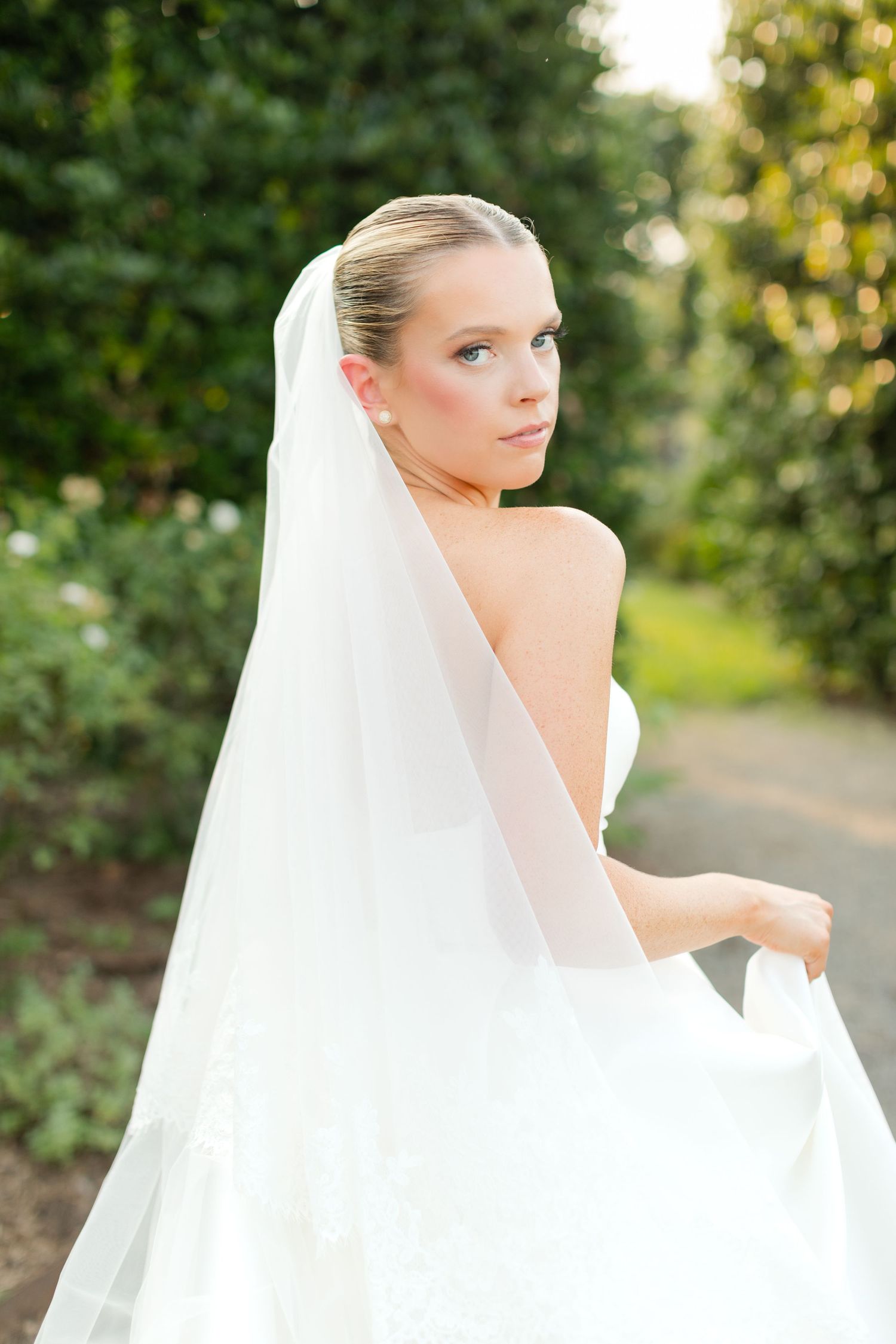A flowing white wedding veil billows gracefully in a garden setting during golden hour.