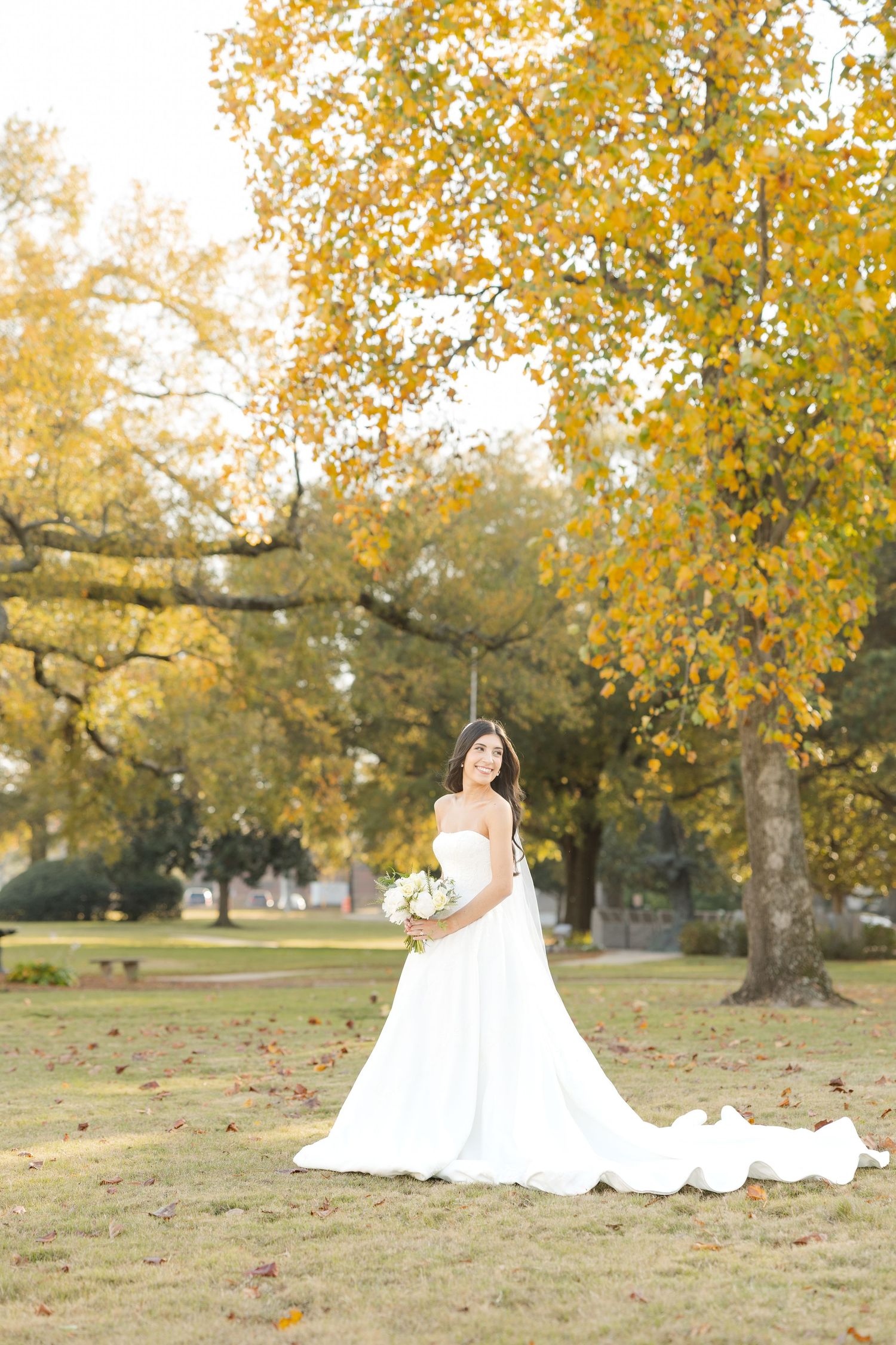 Fall bridal portraits with golden autumn leaves and flowing white wedding dress in a park setting.
