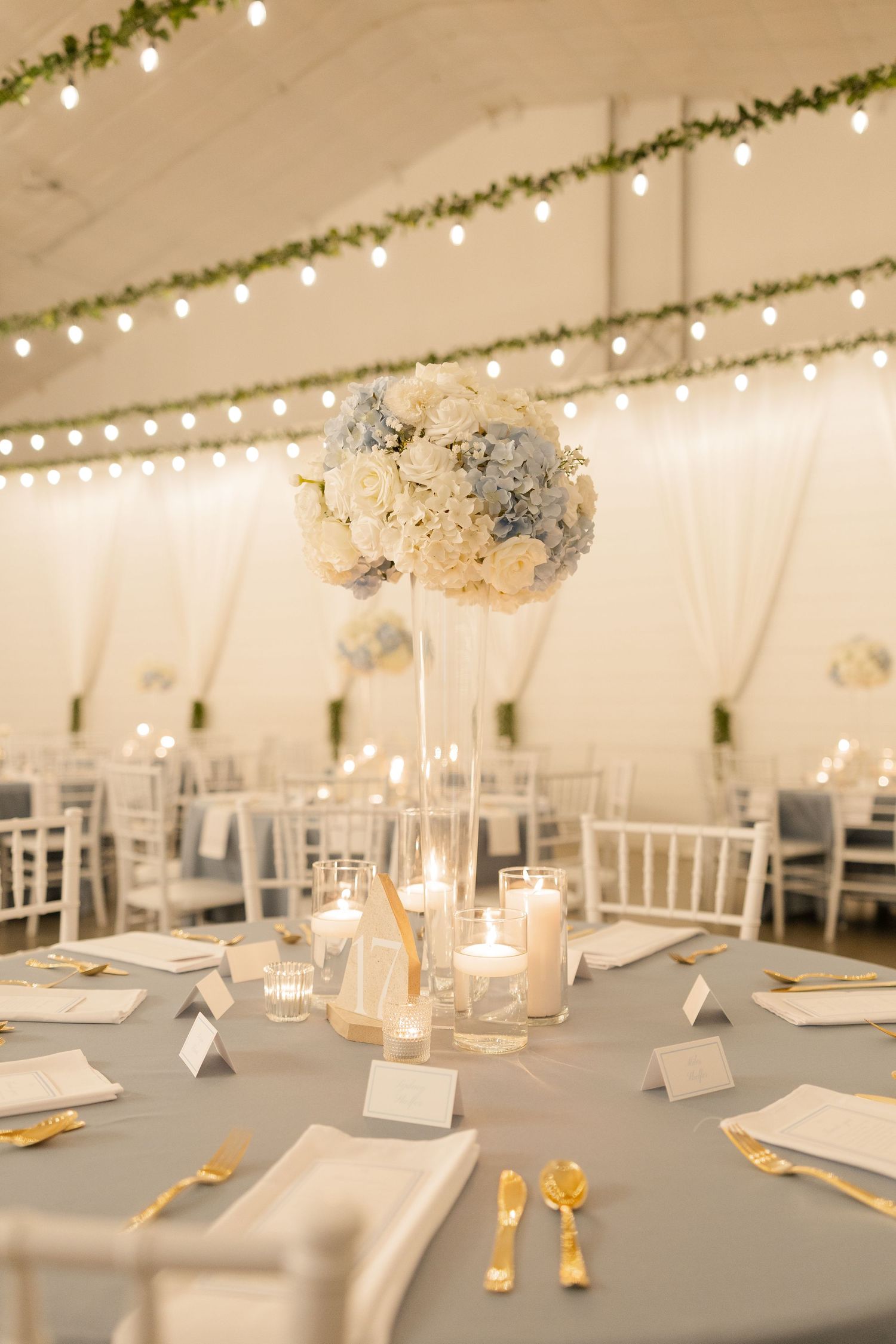 Romantic wedding reception table with tall floral centerpiece, string lights and white tent draping.