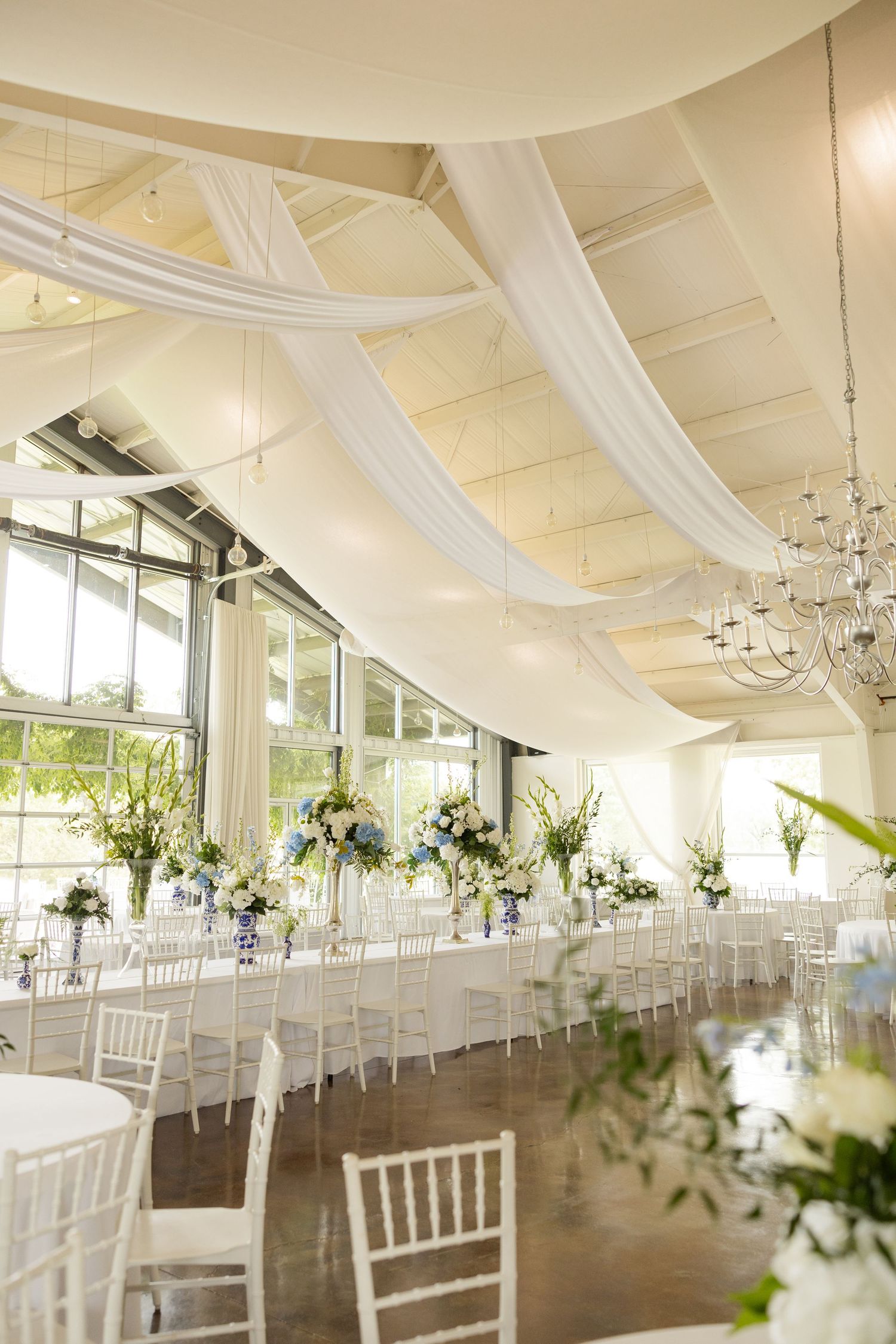 Elegant wedding reception setup with white draping, chandeliers and floral centerpieces.Cold Springs Events
