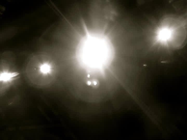 Bright white stage lights shine through darkness creating a dramatic atmospheric effect during a performance.