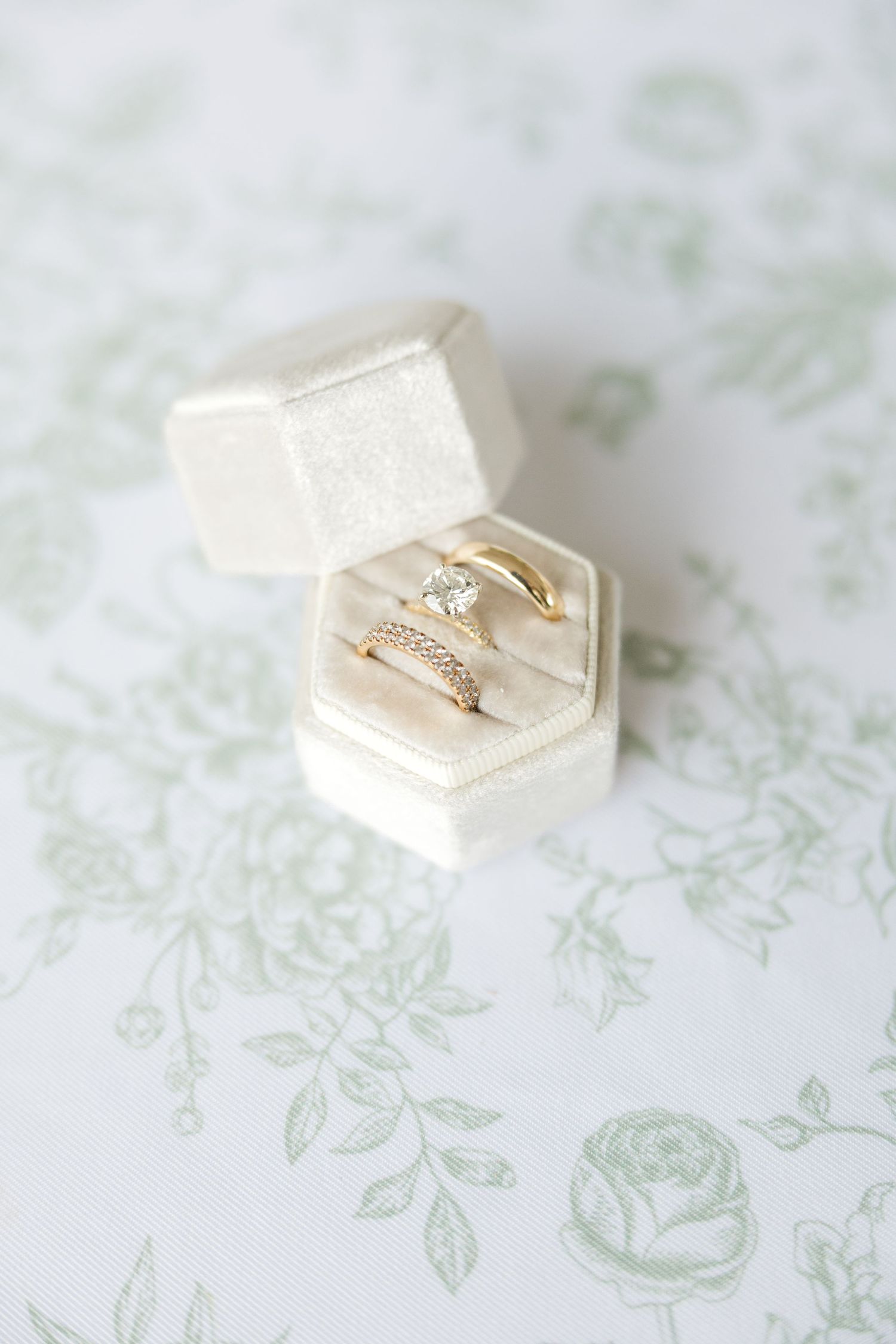 Delicate wedding rings displayed in white hexagonal ring boxes on a floral patterned surface.Botanical Gardens of the Ozarks