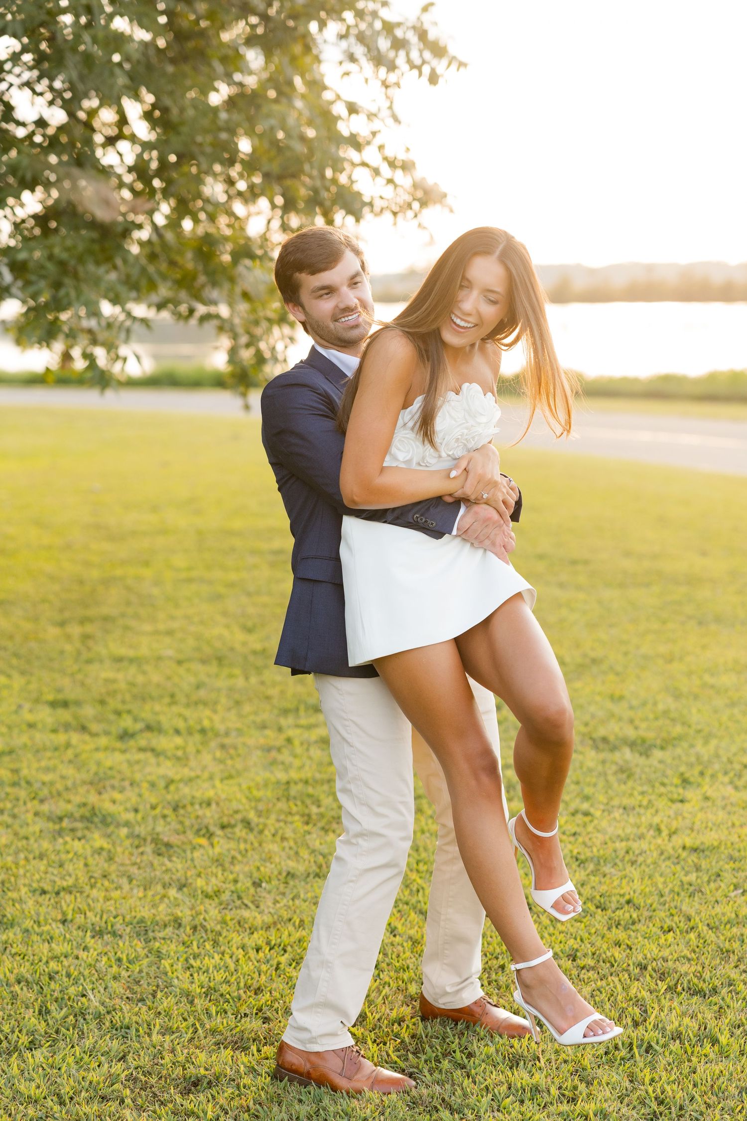 A playful couple laughs together on a sunlit lawn during golden hour.