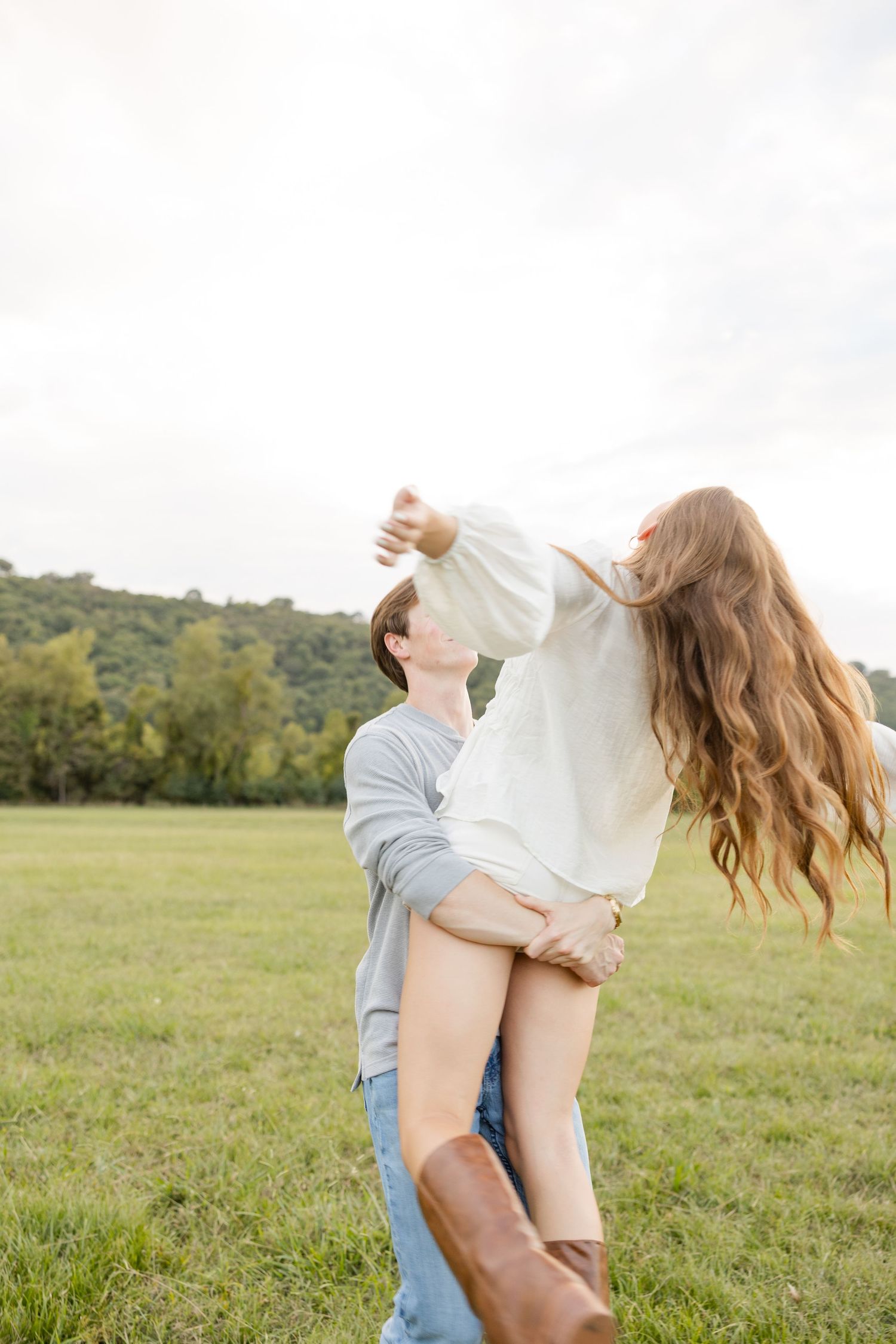 A couple shares a playful moment as they dance and spin in an open field at golden hour.