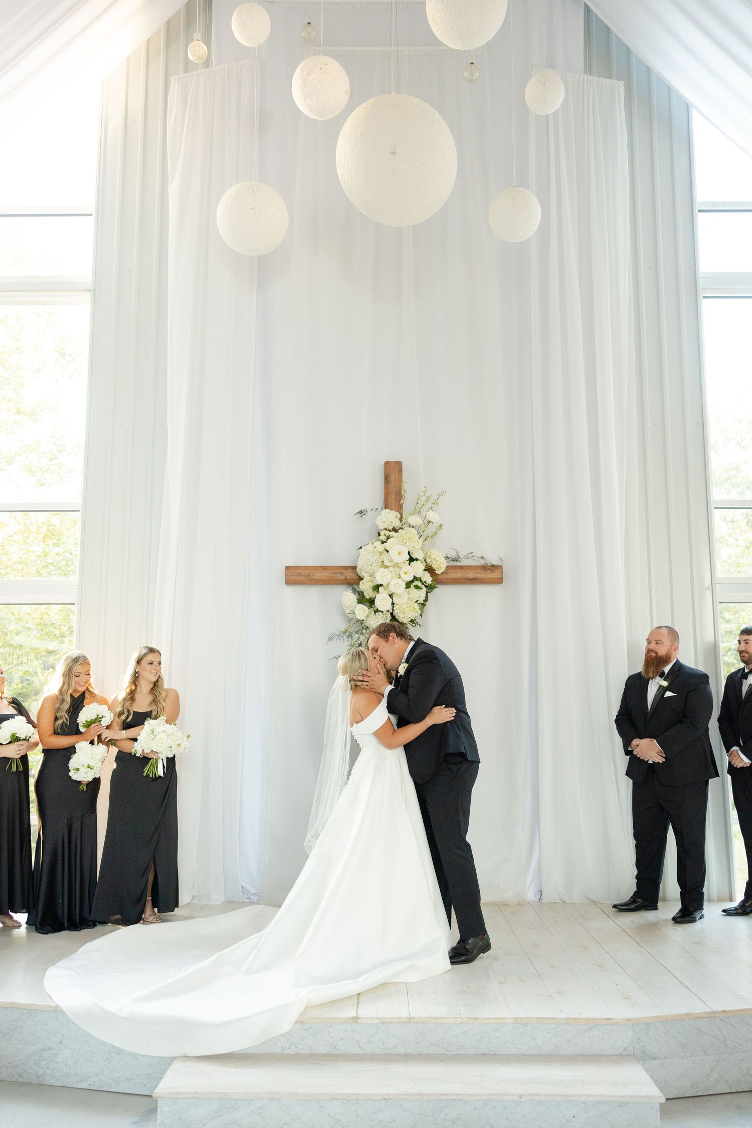 Wedding party stands in elegant white draped room with ethereal decor and soft lighting during ceremony. Cold Springs Events.