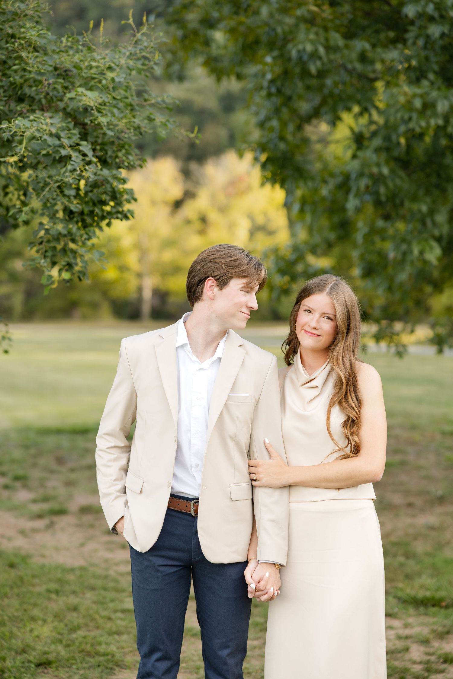 A romantic couple sharing a tender moment in a park setting wearing coordinated beige and white outfits.