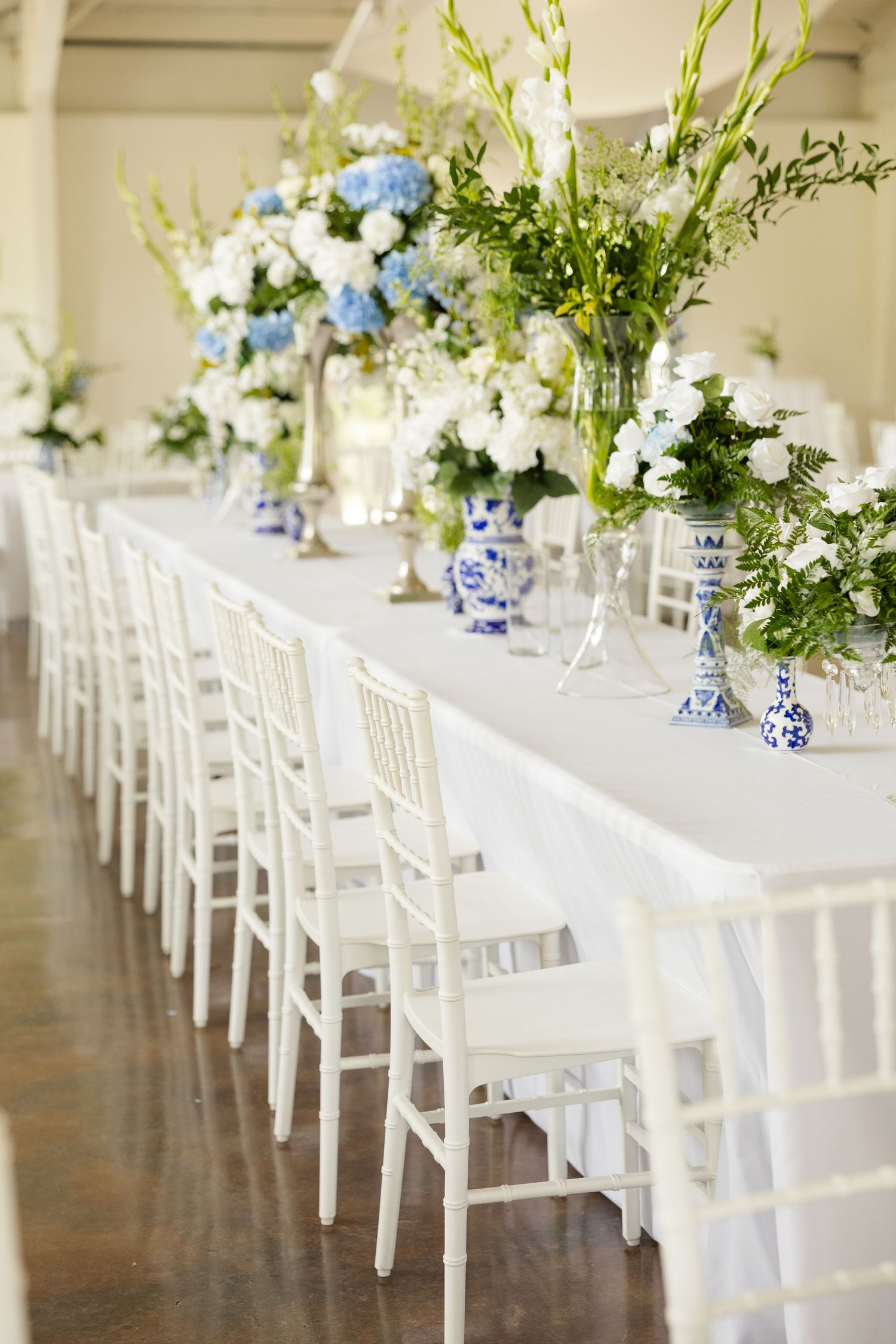 Elegant white wedding reception tables decorated with blue and white floral centerpieces and white chiavari chairs.Cold Springs Events.