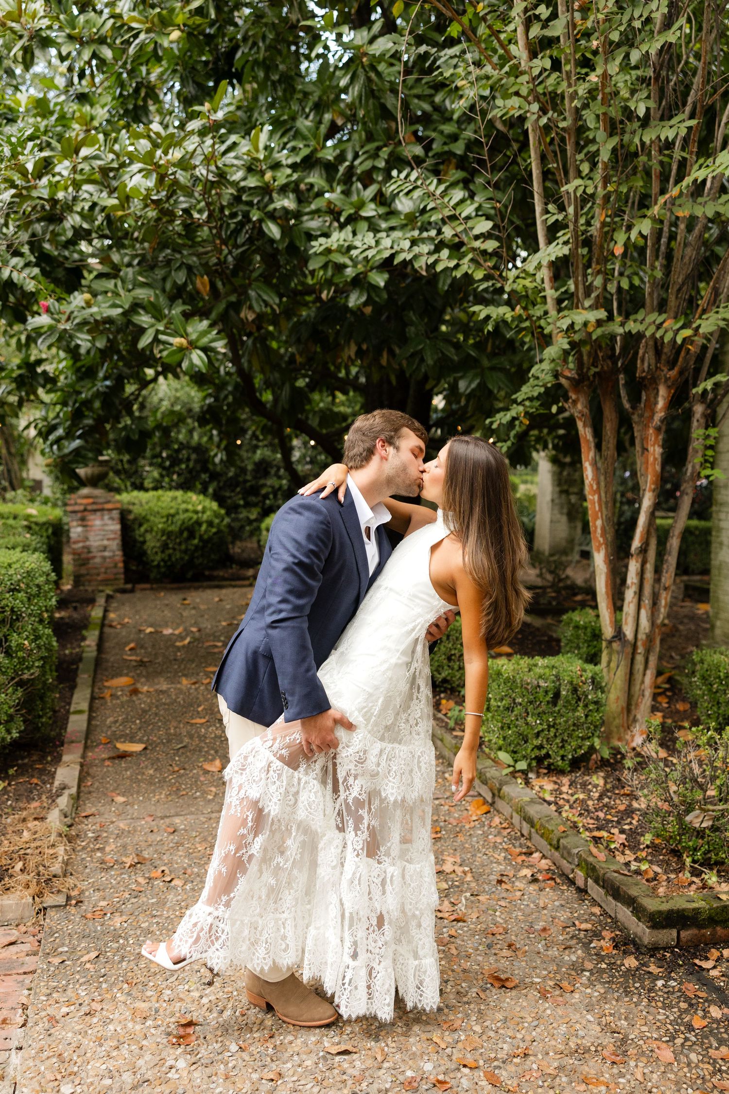 Romantic couple shares tender moments in a garden pathway surrounded by green foliage and brick walls.