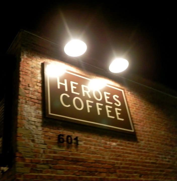 Illuminated neon signage for Heroes Coffee displayed on a rustic brick wall at night.