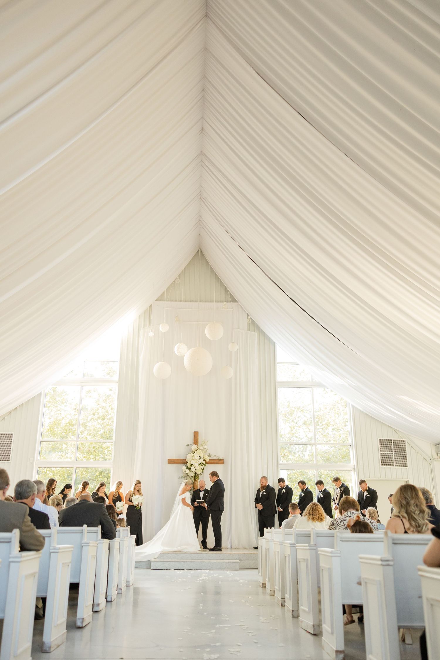Elegant white draped tent interior with rows of white chairs set up for an indoor wedding ceremony.