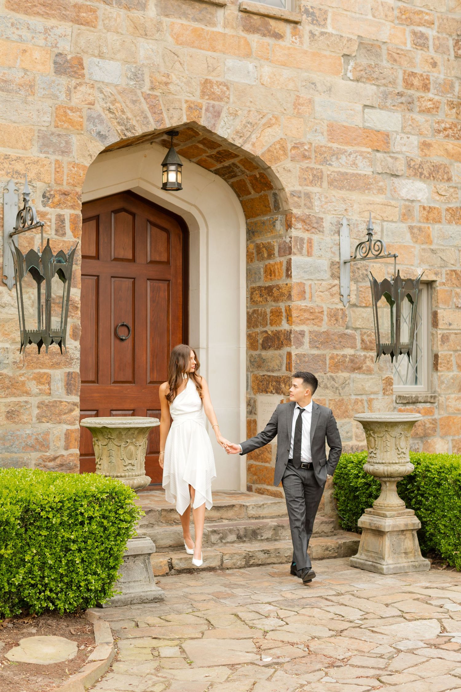 A sequence of romantic photos showing a couple walking along a stone building exterior with vintage lanterns. Goodwin Manor.