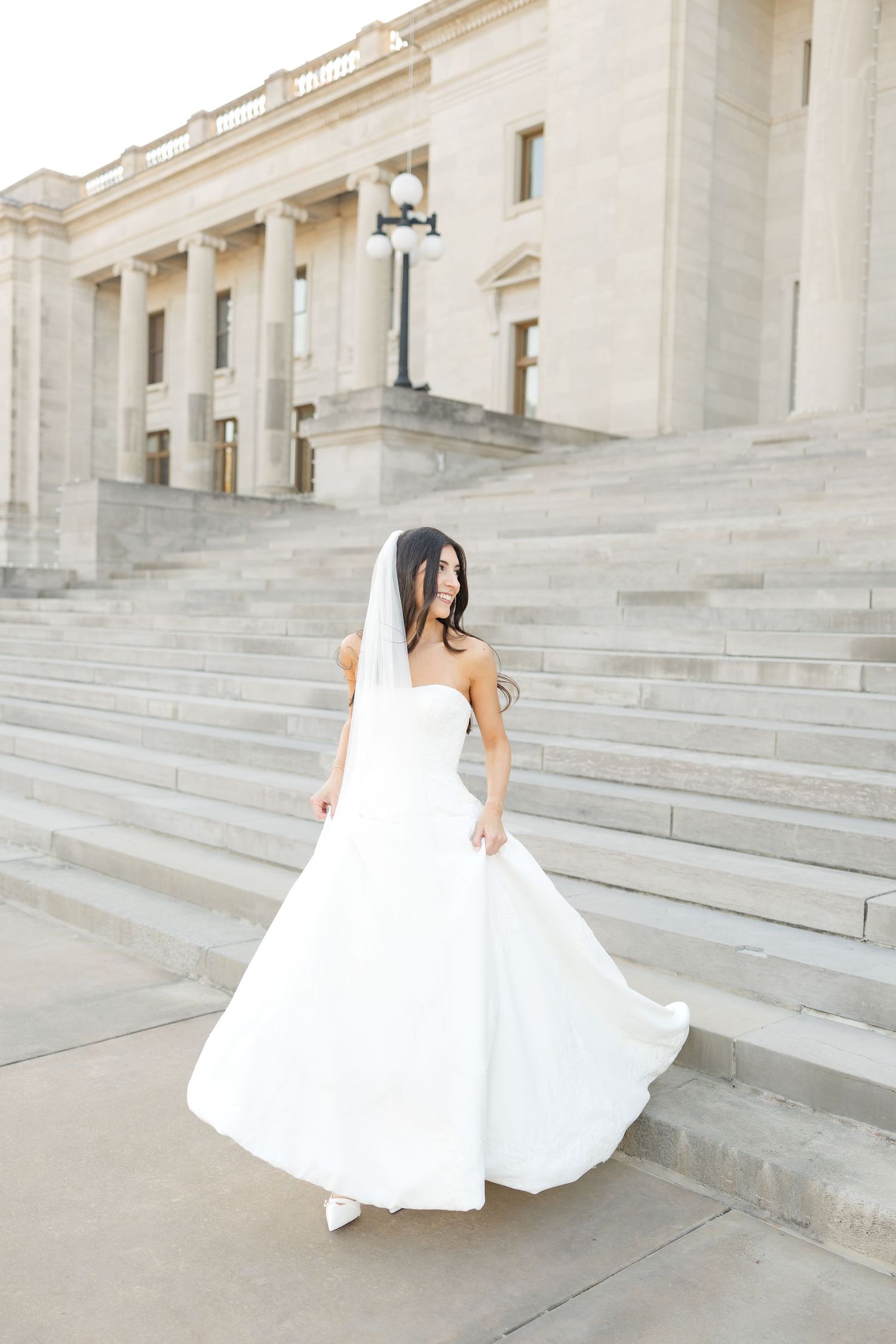 A flowing white wedding dress twirls gracefully on the grand stone steps of a neoclassical building.