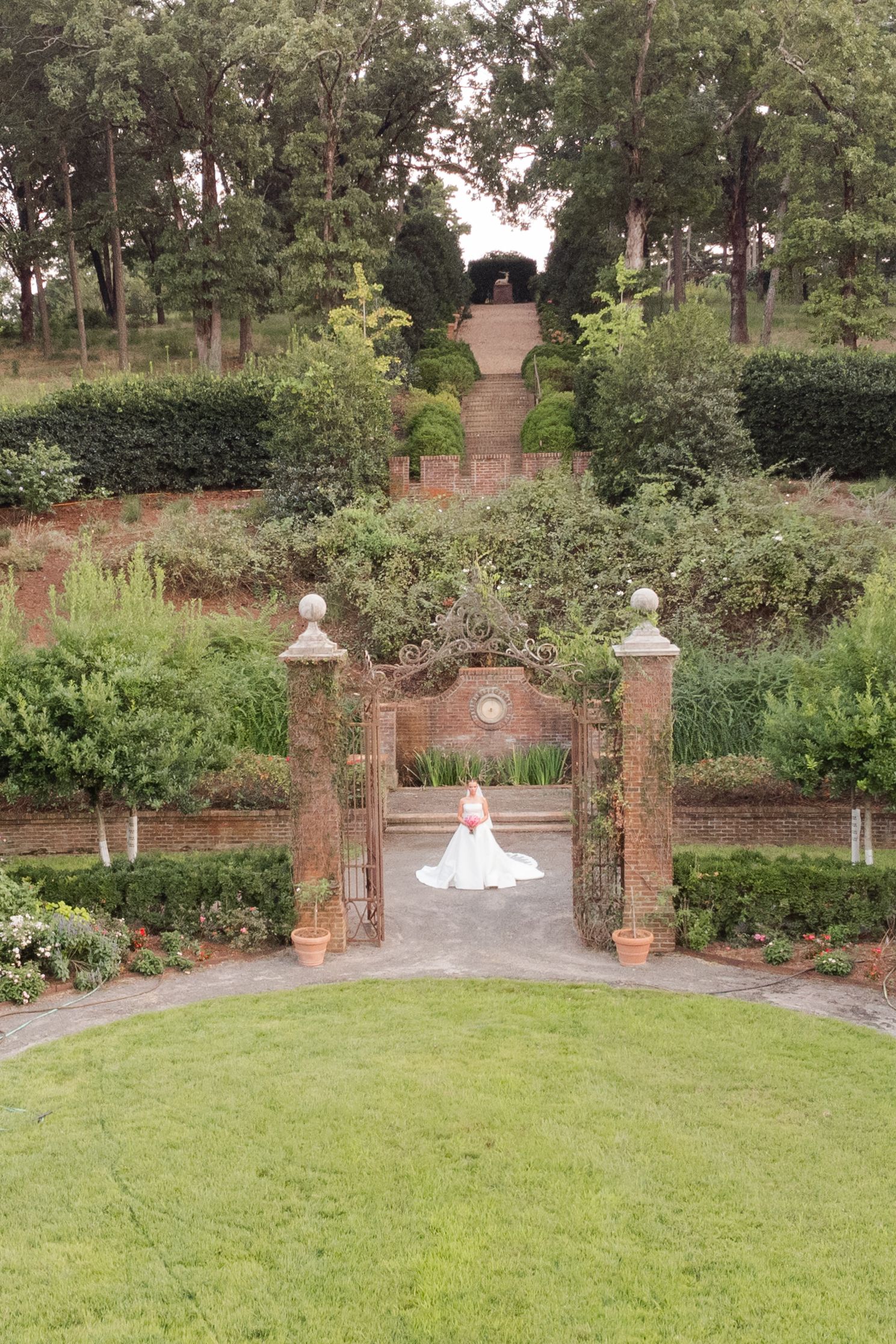 Panoramic view of a formal garden with brick pillars, ornamental statues, and a well-maintained green lawn.