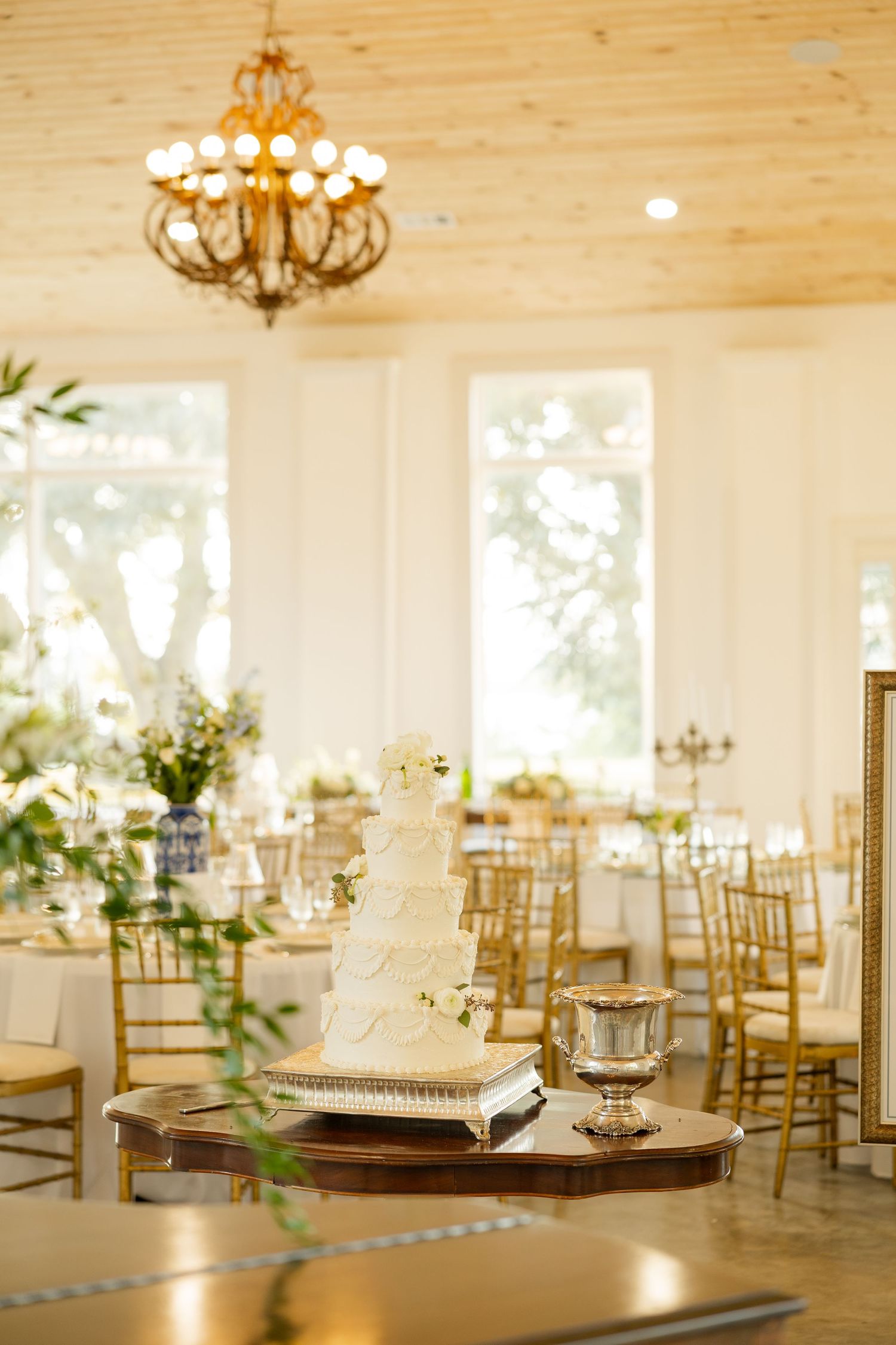 Light-filled wedding reception room with wooden ceiling, chandeliers and gold chiavari chairs.